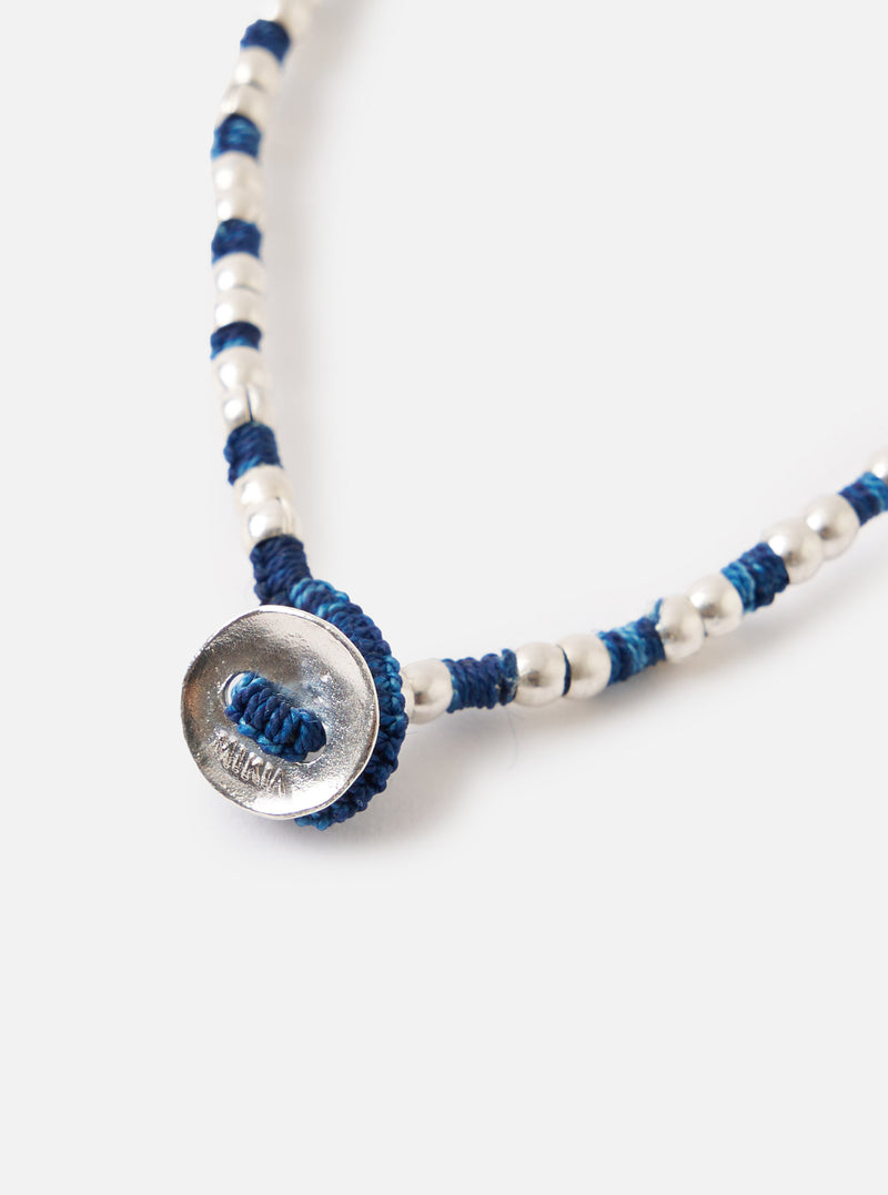 Close-up of a Mikia Indigo Silver Beads Bracelet on a white surface. The bracelet features indigo thread and silver beads, secured with a silver button clasp.