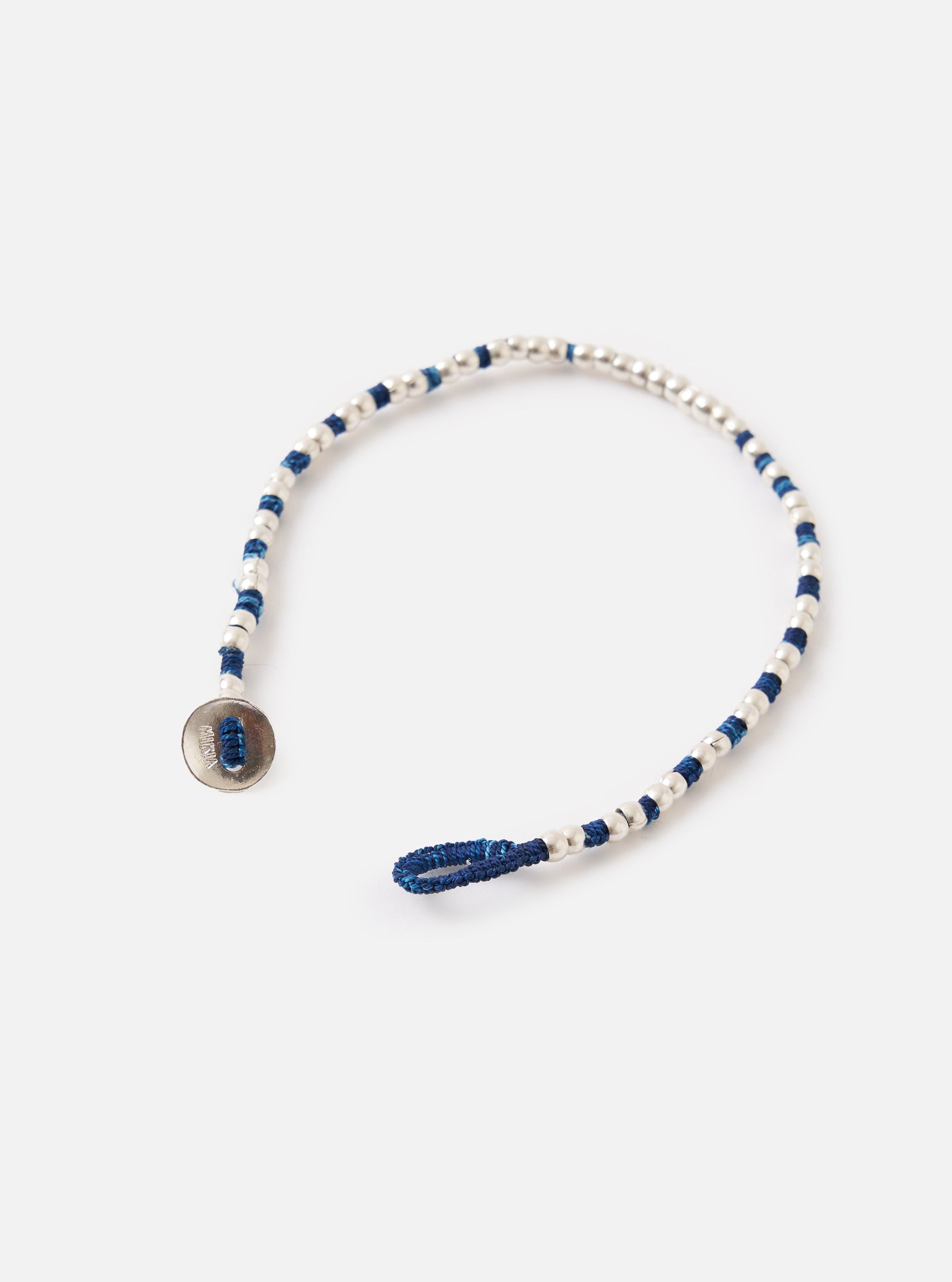 The Mikia Indigo Silver Beads Bracelet on a white surface. The bracelet features indigo thread and silver beads. It has a button closure.