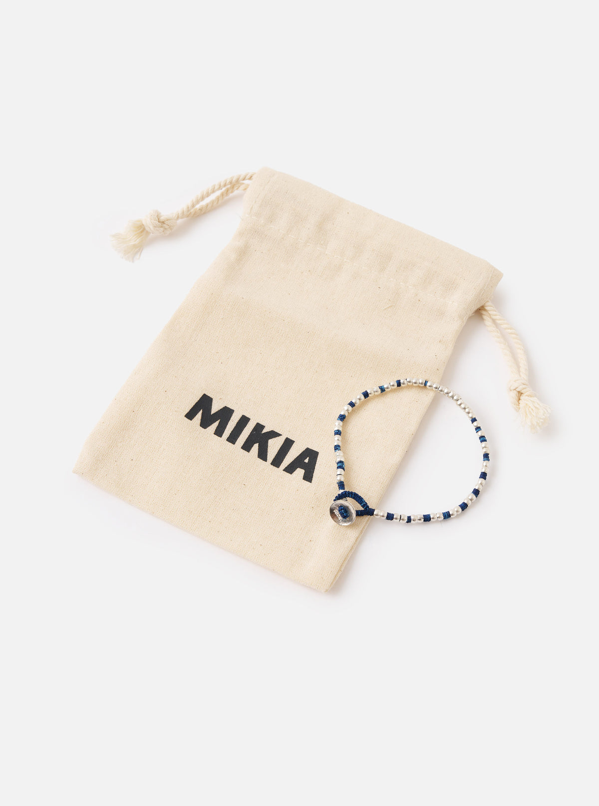 The Mikia Indigo Silver Beads Bracelet next to its branded pouch on a white surface. The bracelet features indigo thread and silver beads.
