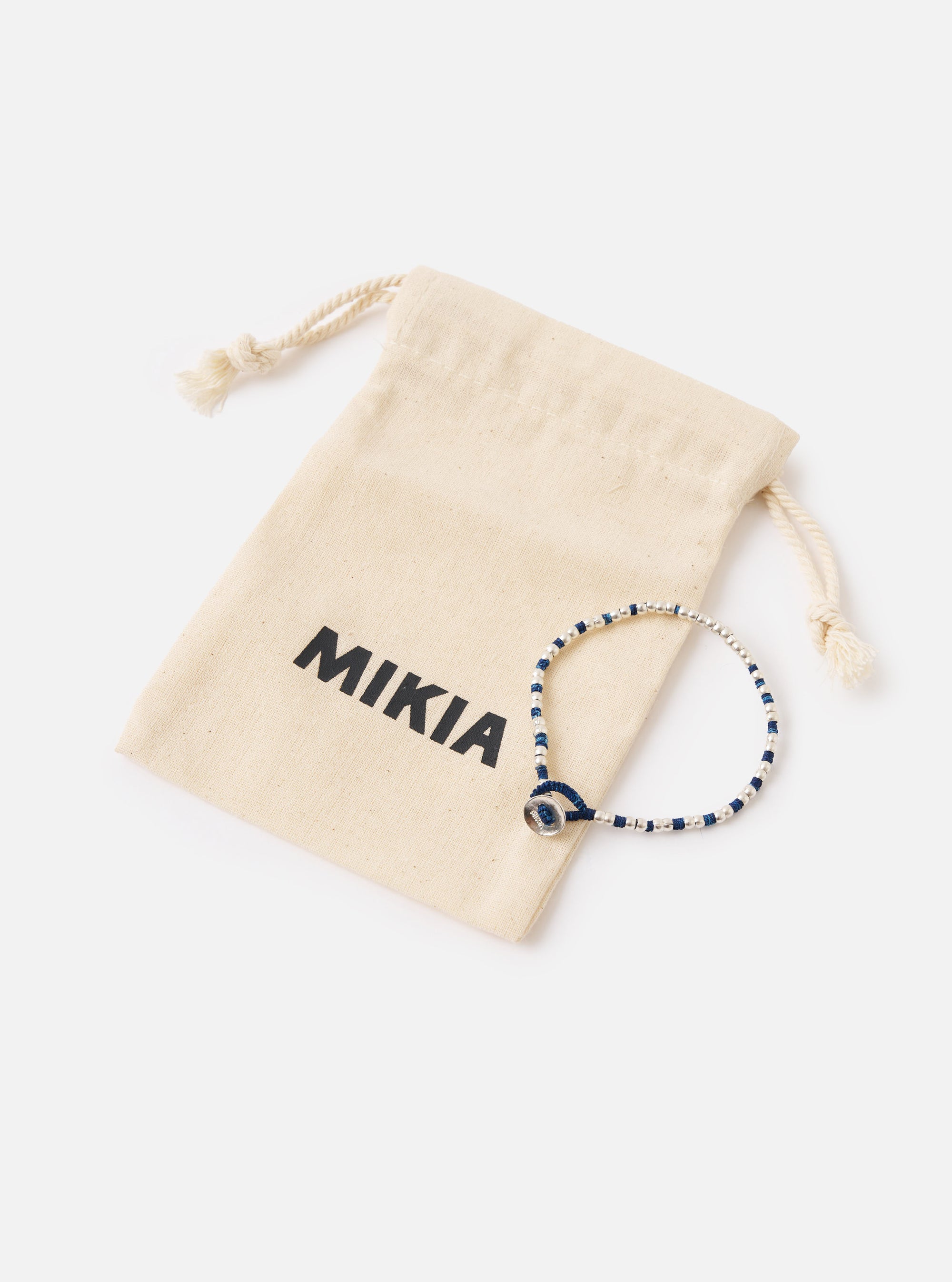 The Mikia Indigo Silver Beads Bracelet next to its branded pouch on a white surface. The bracelet features indigo thread and silver beads.