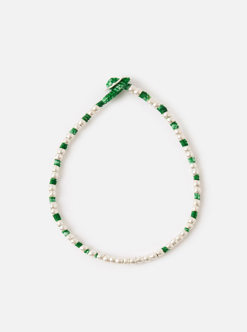 The Mikia Malachite Silver Beads Bracelet on a white surface. The bracelet features green thread and silver beads. 