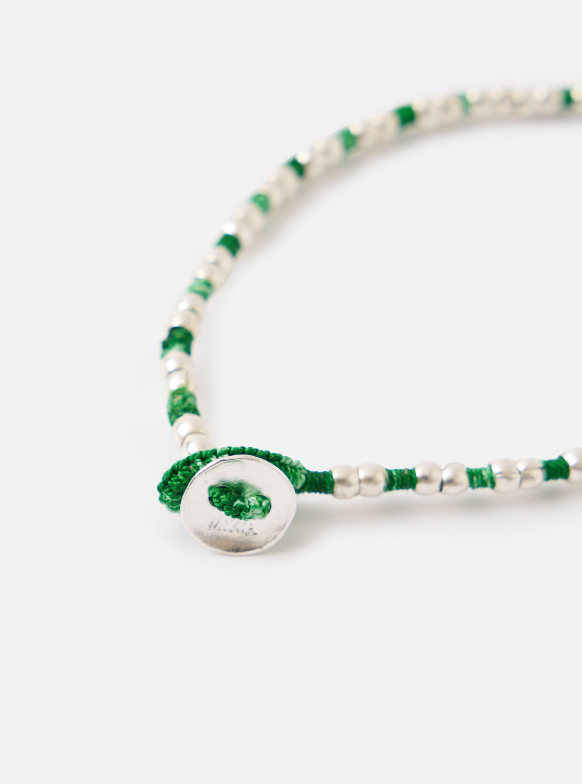 Close-up of the Mikia Malachite Silver Beads Bracelet on a white surface. Features silver beads with green thread and a silver button clasp.