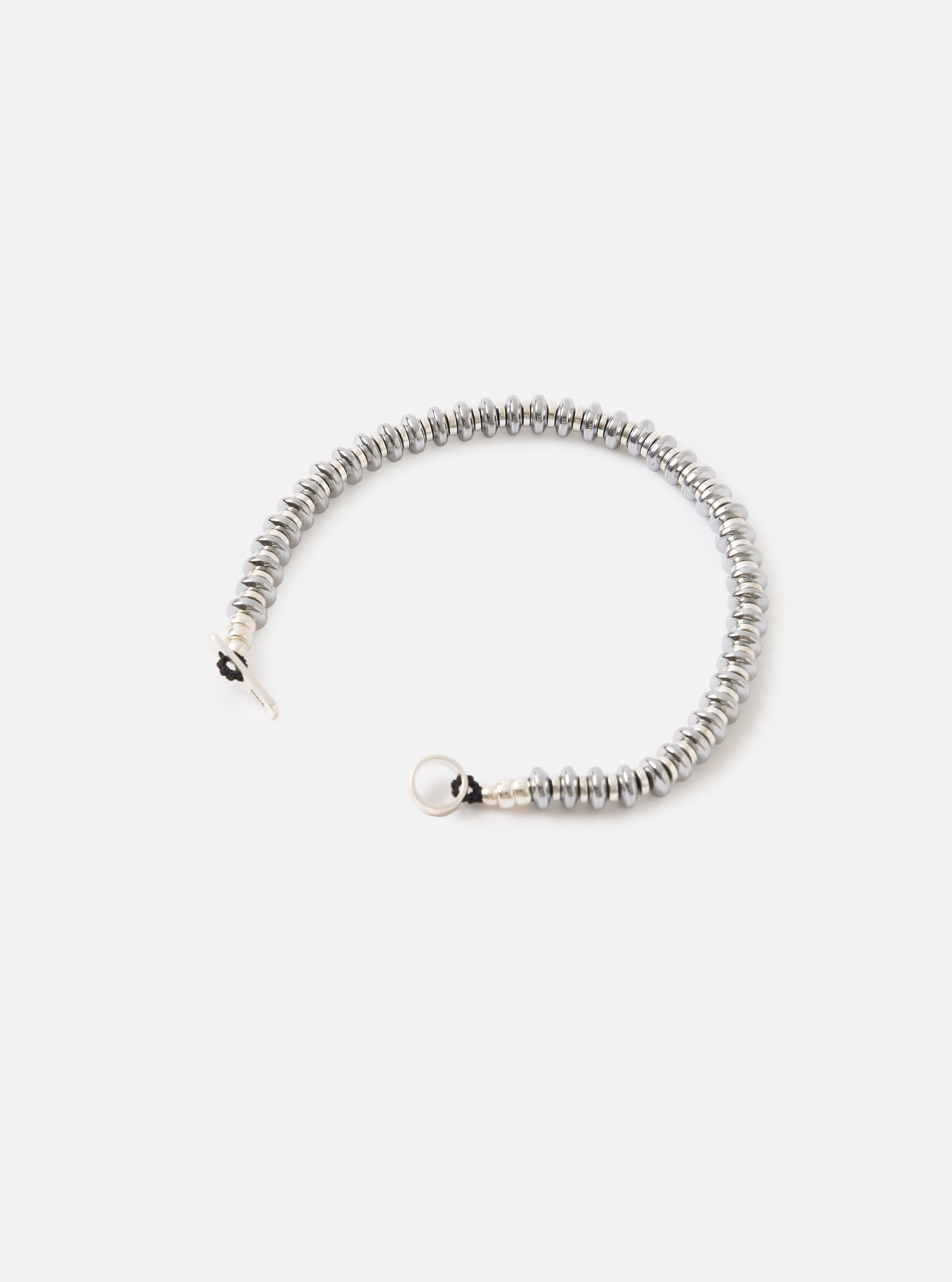 The Mikia Hematite Roundel Bracelet on a white surface. The bracelet is made of hematite roundels and has a silver clasp. The background is plain white.