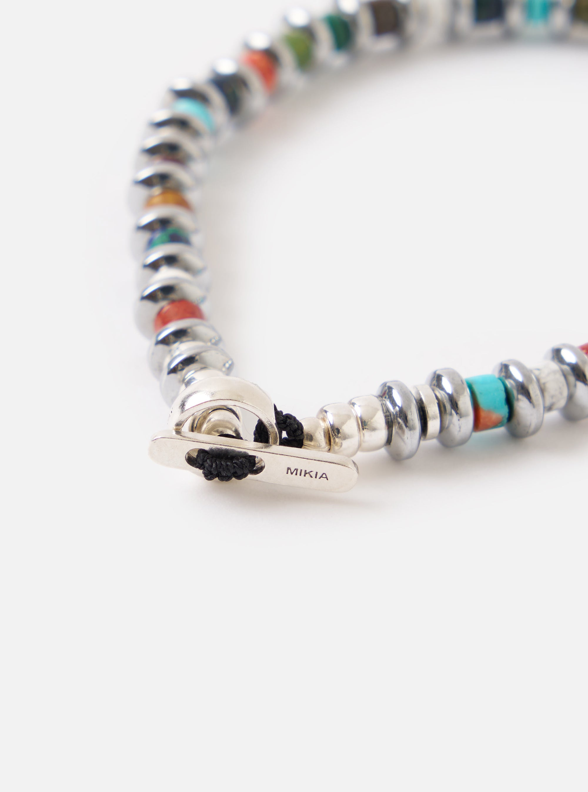 Close-up of the Mikia Multi Hematite Roundel Bracelet on a white surface. The bracelet features silver roundels and colorful beads. The clasp is visible, showcasing the Mikia logo.