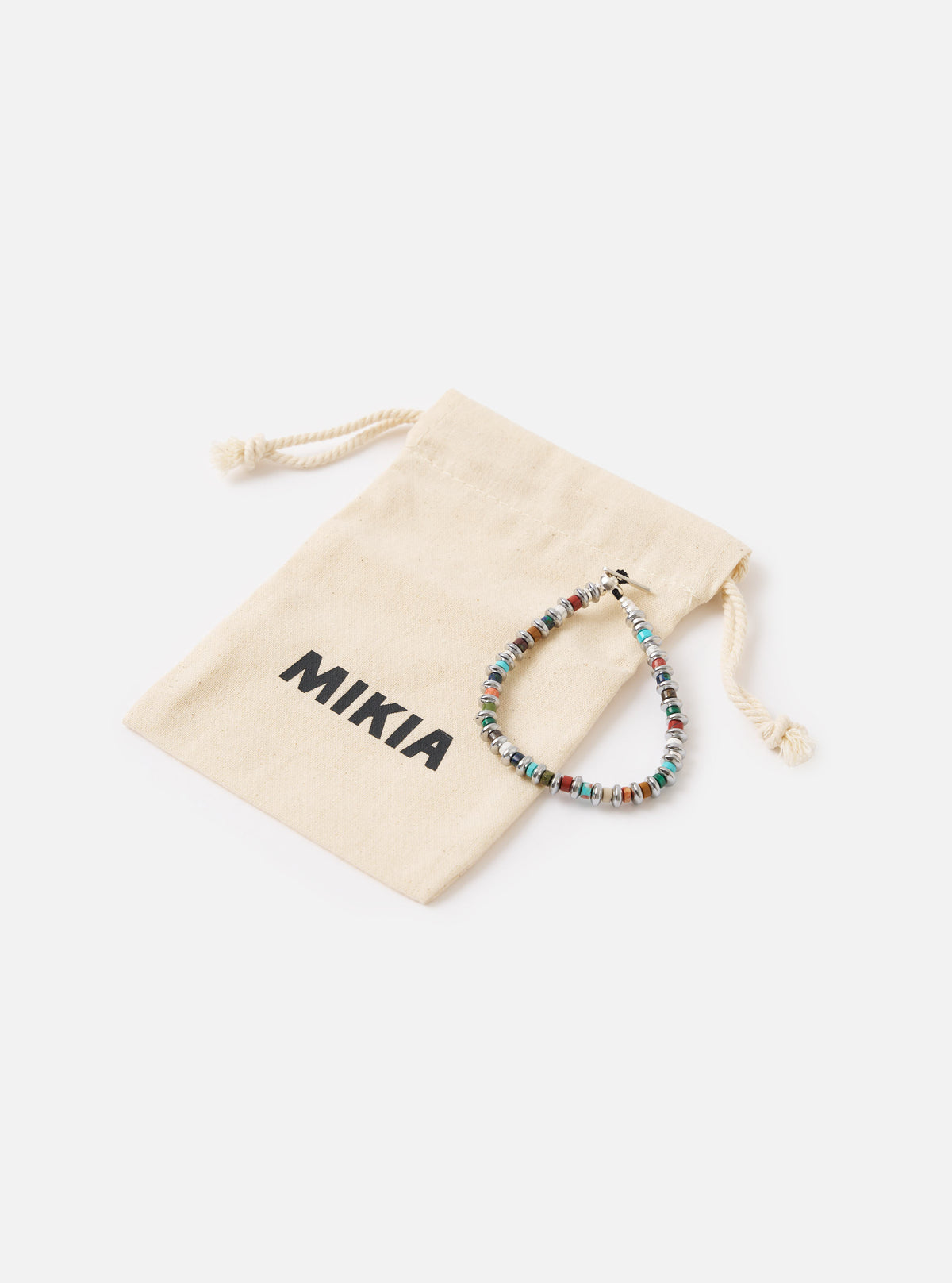The Mikia Multi Hematite Roundel Bracelet on a white surface next to its branded pouch. The bracelet features colorful stones and silver accents.