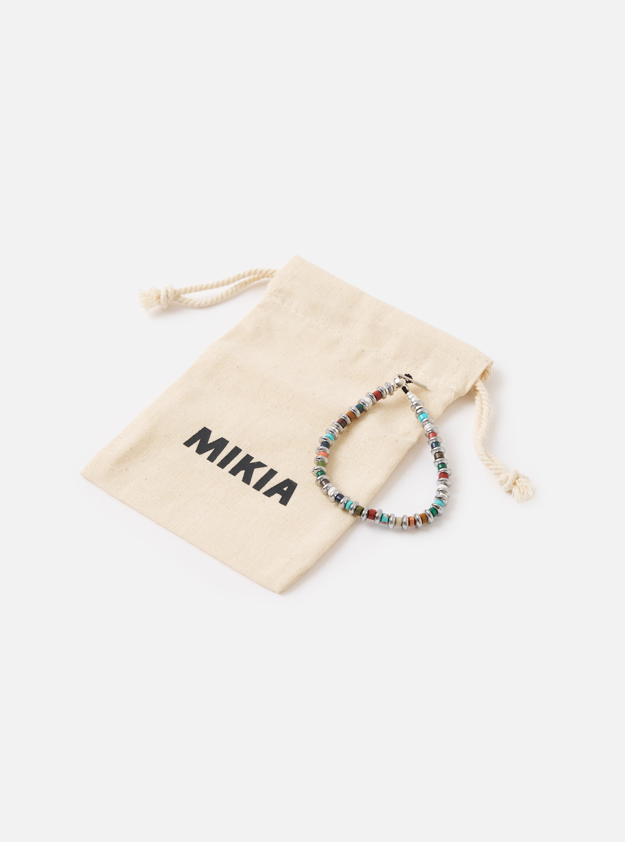 The Mikia Multi Hematite Roundel Bracelet on a white surface next to its branded pouch. The bracelet features colorful stones and silver accents.