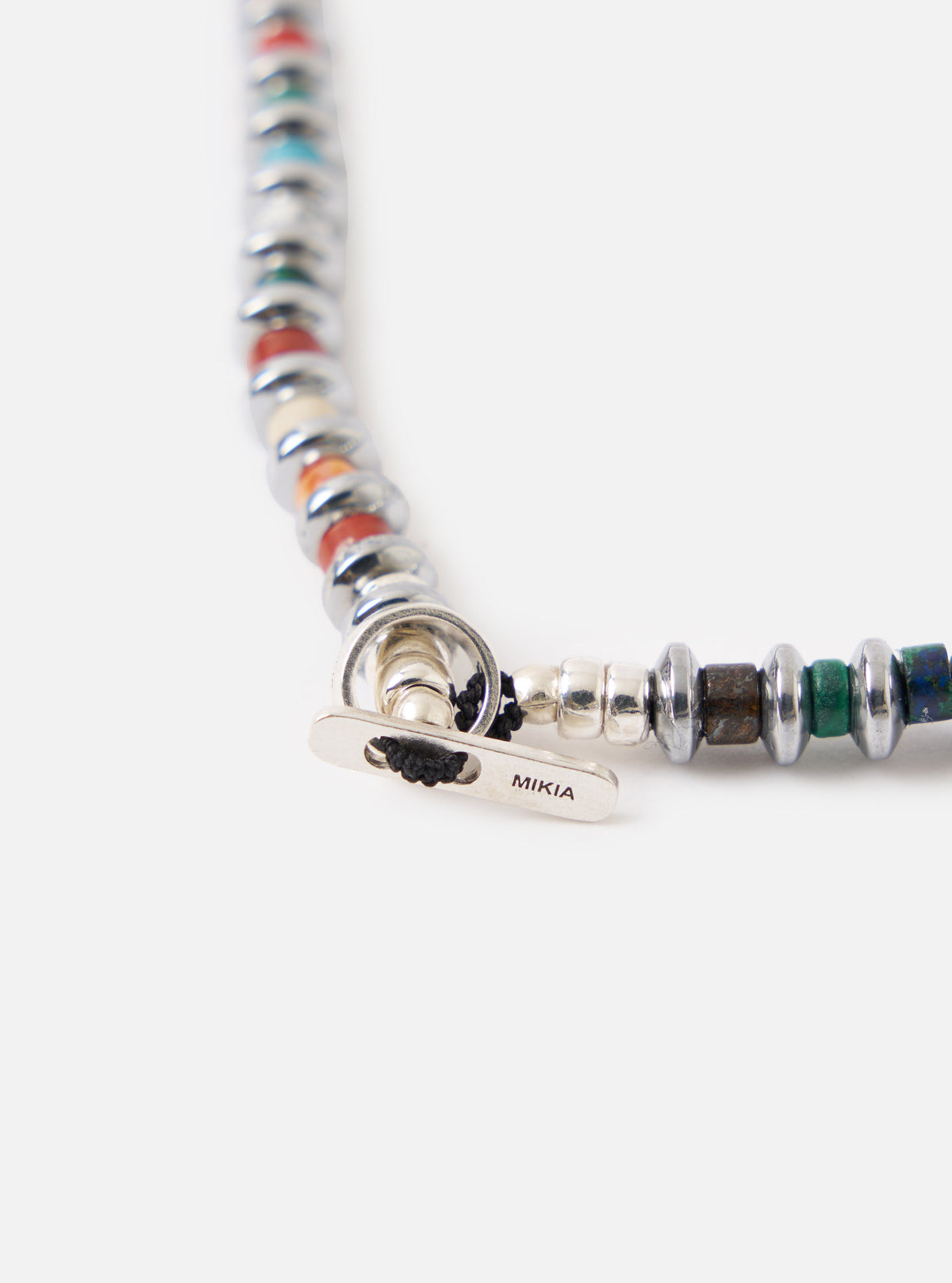 Close-up of the Mikia Multi Hematite Roundel Necklace on a white surface. Features colorful roundels and silver hardware.
