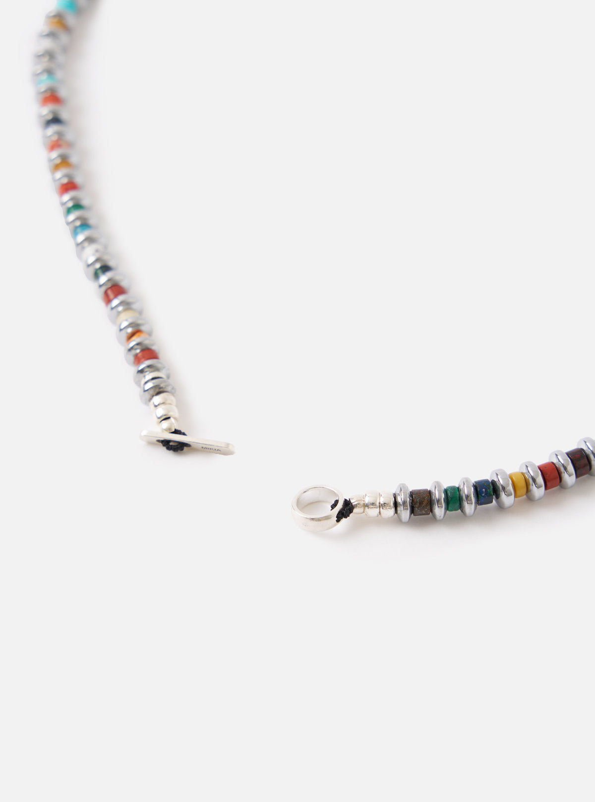 Close-up of the Mikia Multi Hematite Roundel Necklace on a white surface. Features colorful roundel beads and silver hematite accents. The necklace is unclasped.