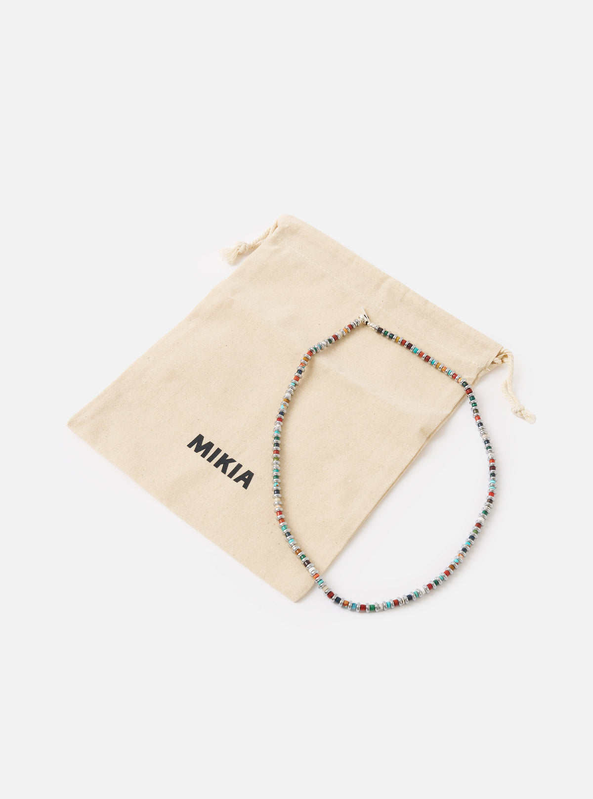The Mikia Multi Hematite Roundel Necklace on a white surface with its branded beige pouch. The necklace features colorful roundel beads.