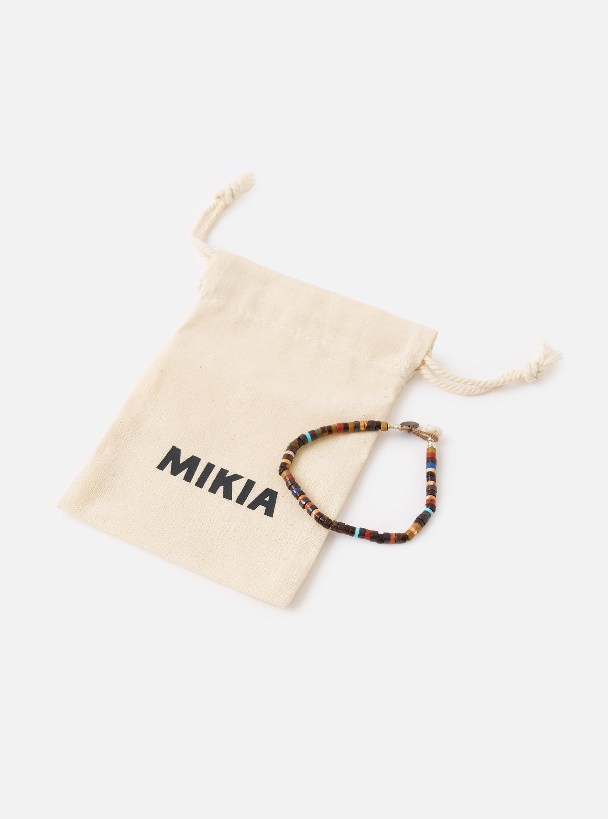 The Mikia Brown Multi Heishi Beads Bracelet on a white surface next to its branded pouch. The bracelet features brown, red, and blue beads.