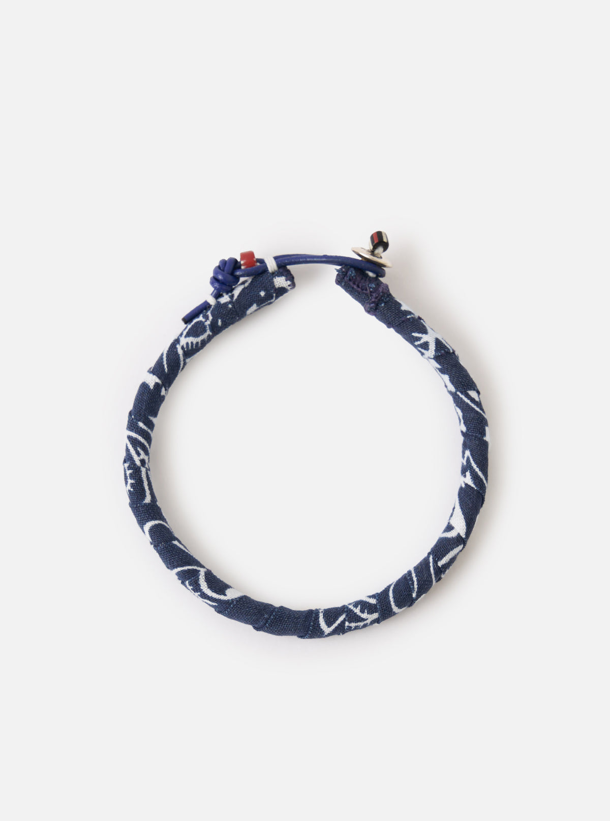 The Mikia Navy Bandana Bracelet on a white surface. The bracelet is made of navy fabric with a white pattern and has a blue leather closure.