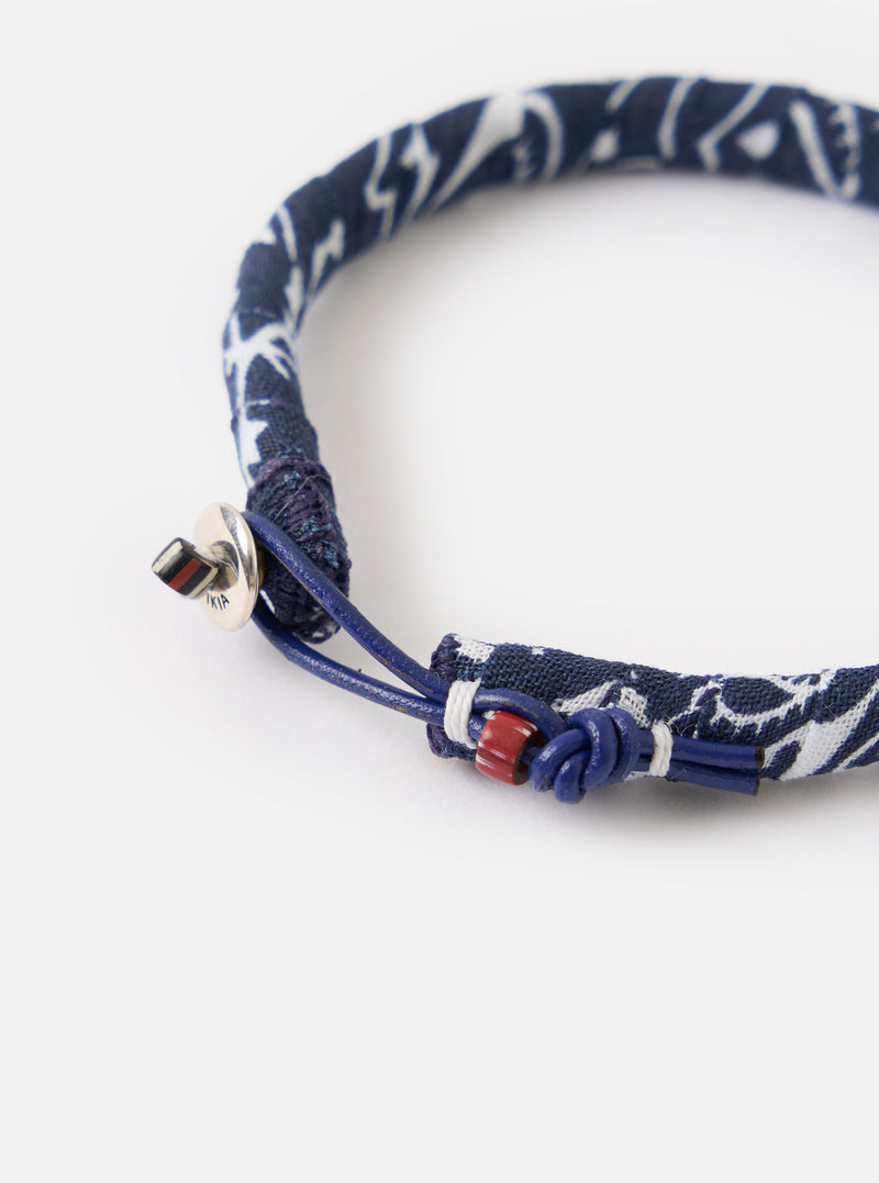 Close-up of the Mikia Navy Bandana Bracelet on a white surface. The bracelet features a blue and white bandana print with a blue leather cord and silver clasp.