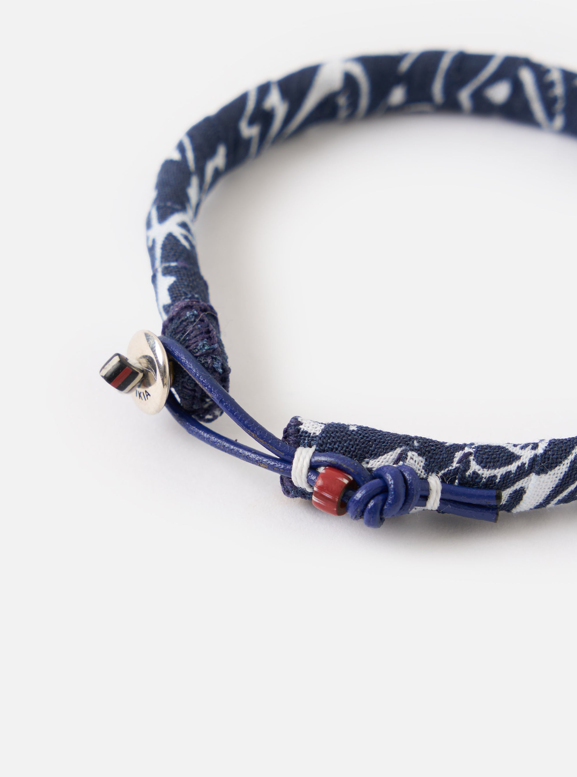 Close-up of the Mikia Navy Bandana Bracelet on a white surface. The bracelet features a blue and white bandana print with a blue leather cord and silver clasp.