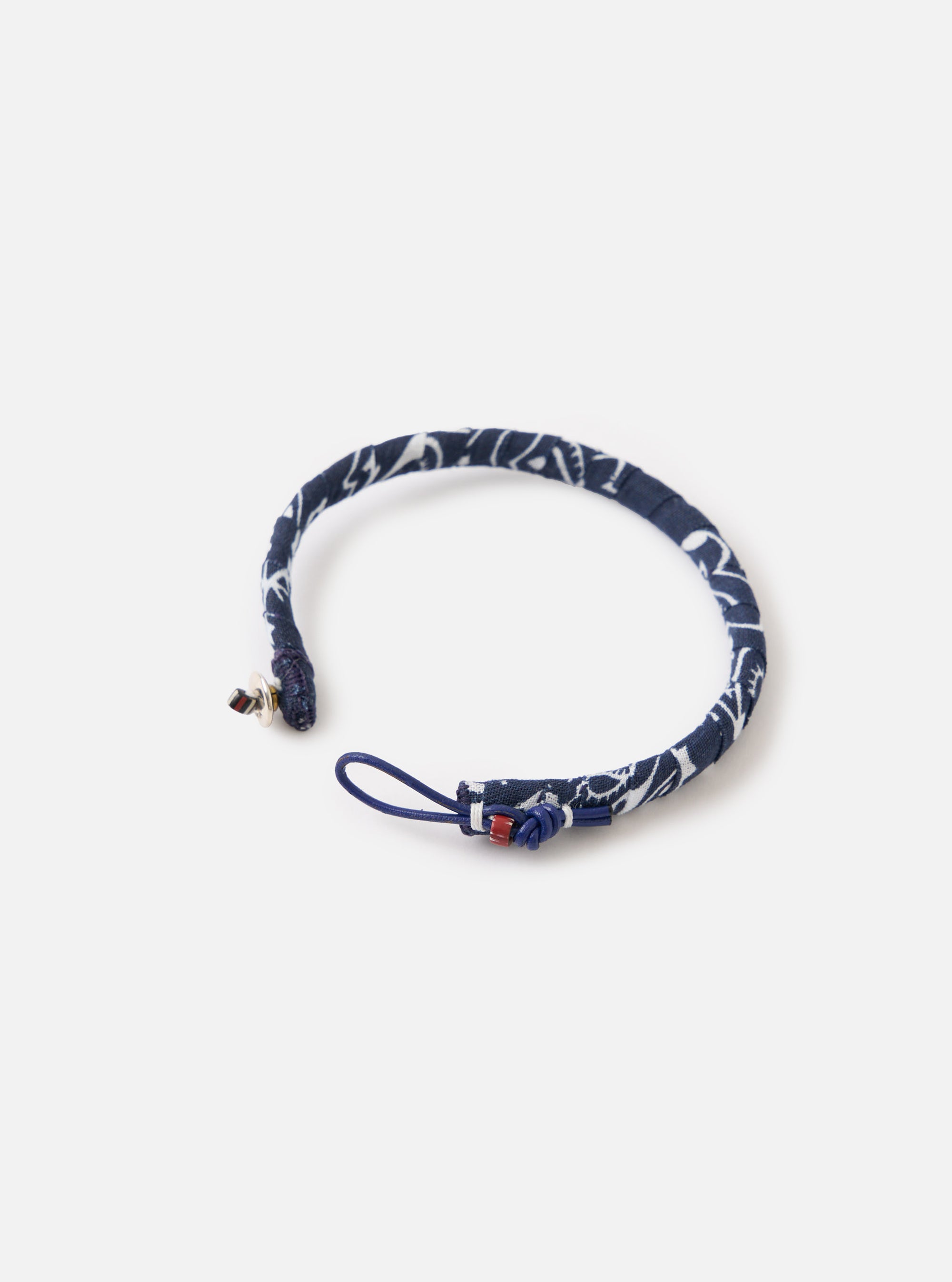 The Mikia Navy Bandana Bracelet on a white surface. The bracelet is navy with a white pattern and has a blue loop and silver clasp. 
