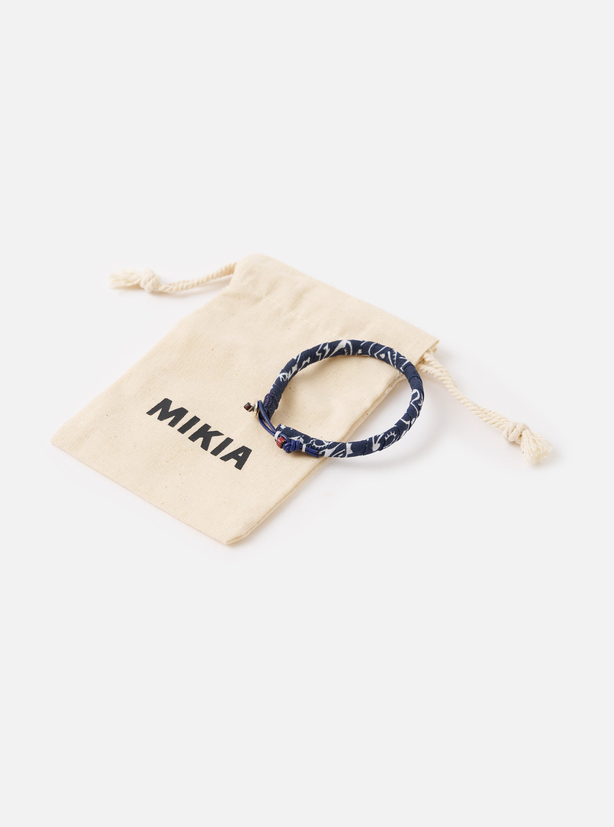 The Mikia Navy Bandana Bracelet on a white surface next to its branded dust bag. The bracelet is navy with a white pattern.