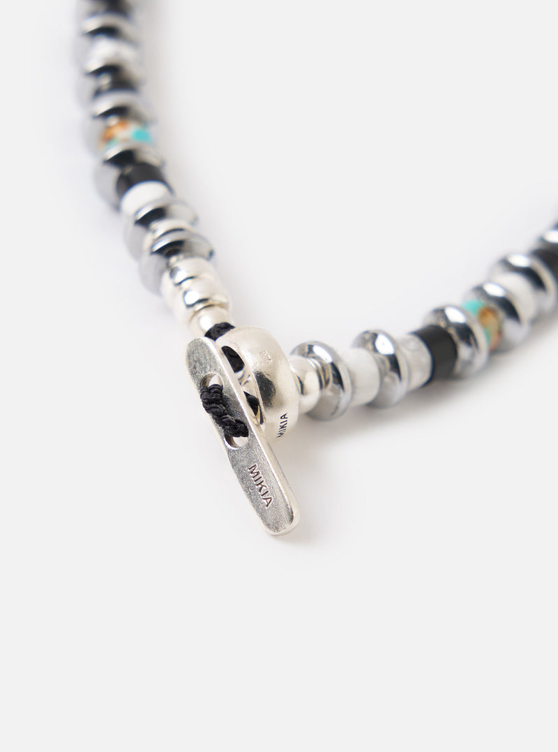 Close-up of the Mikia Jet/Turquoise Hematite Roundel Bracelet on a white surface. Features hematite, turquoise, and a silver clasp. 