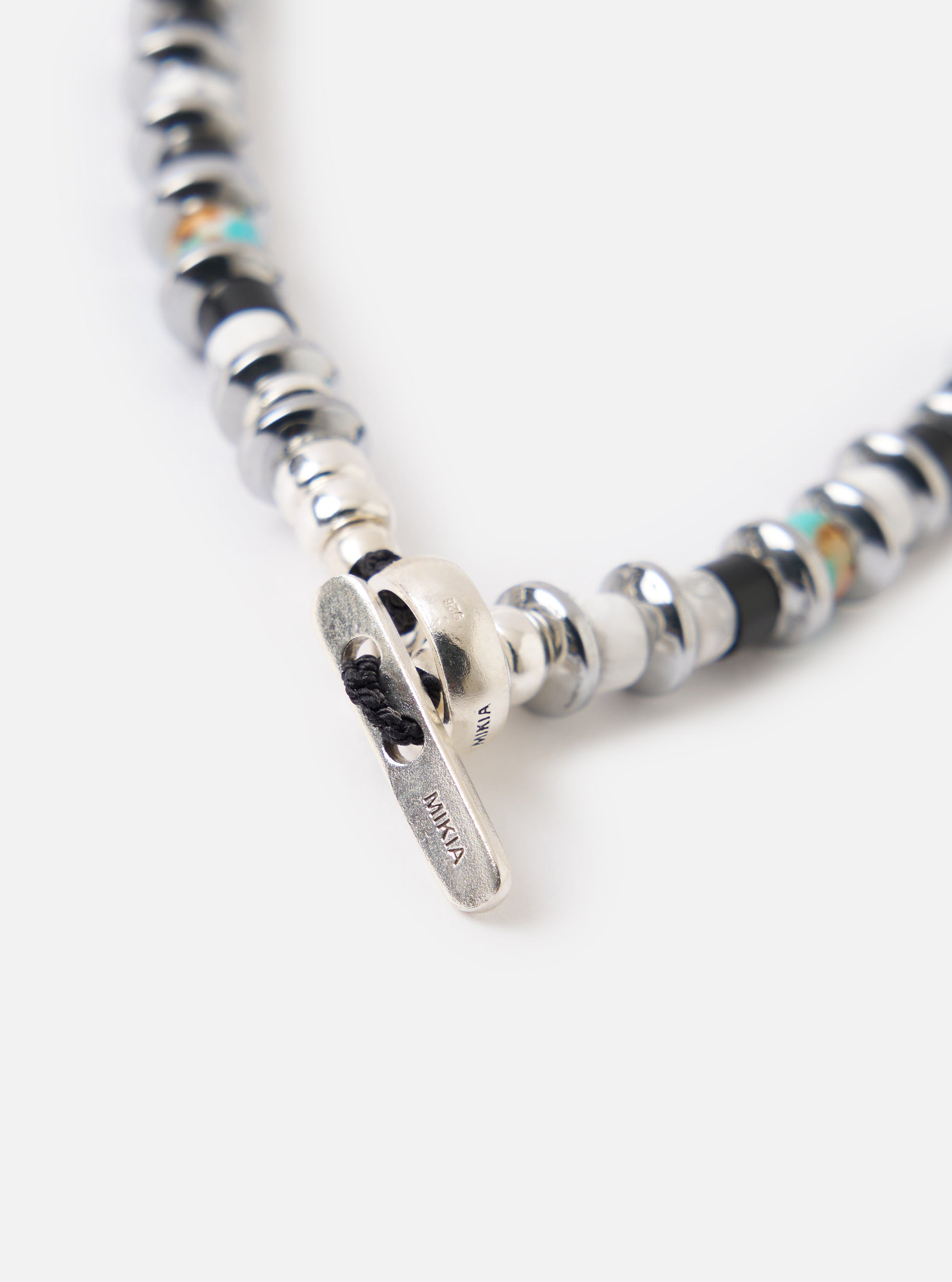 Close-up of the Mikia Jet/Turquoise Hematite Roundel Bracelet on a white surface. Features hematite, turquoise, and a silver clasp. 