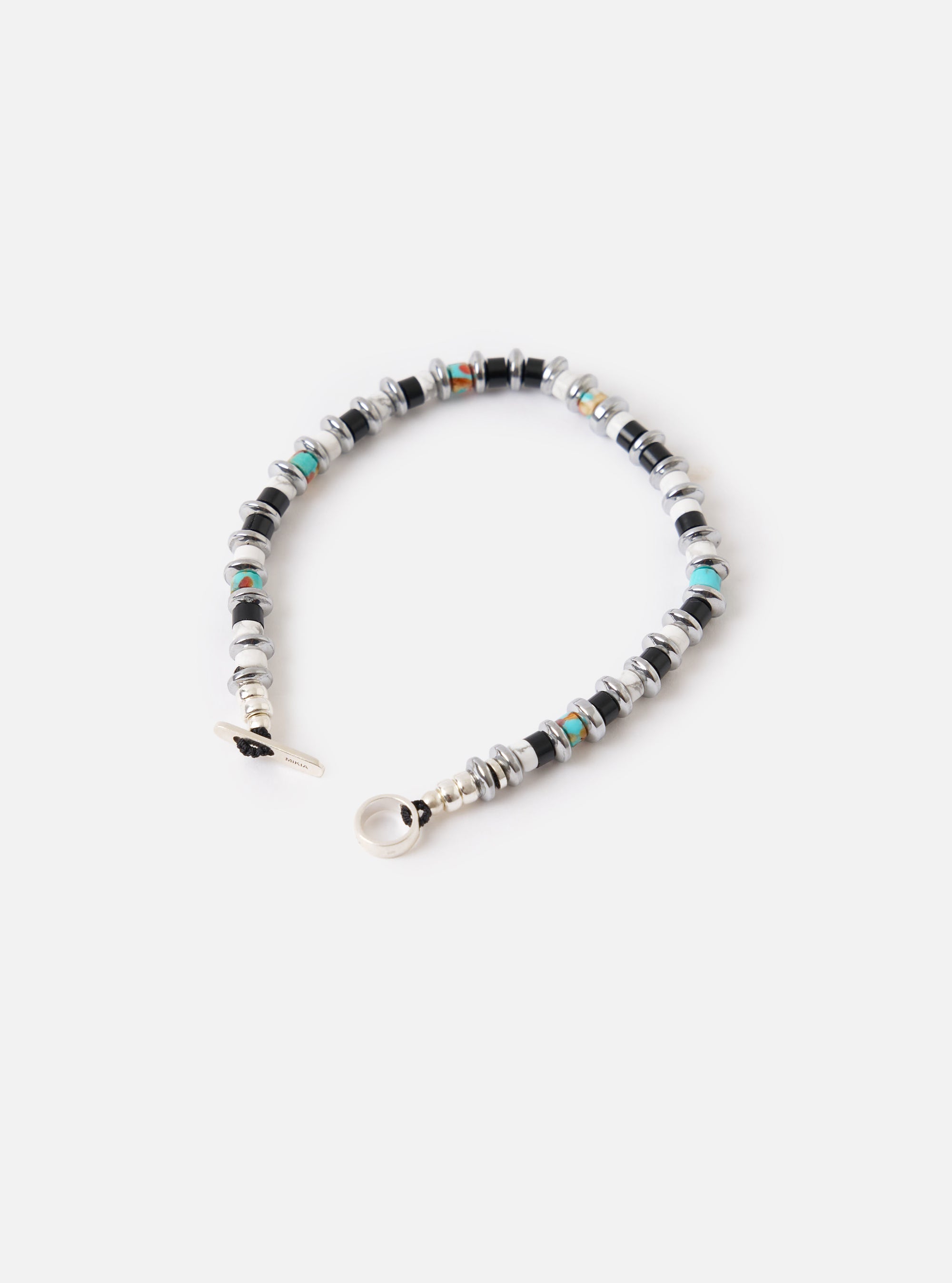 The Mikia Jet/Turquoise Hematite Roundel Bracelet on a white surface. It features jet black, turquoise, and hematite beads. The bracelet has a toggle closure.