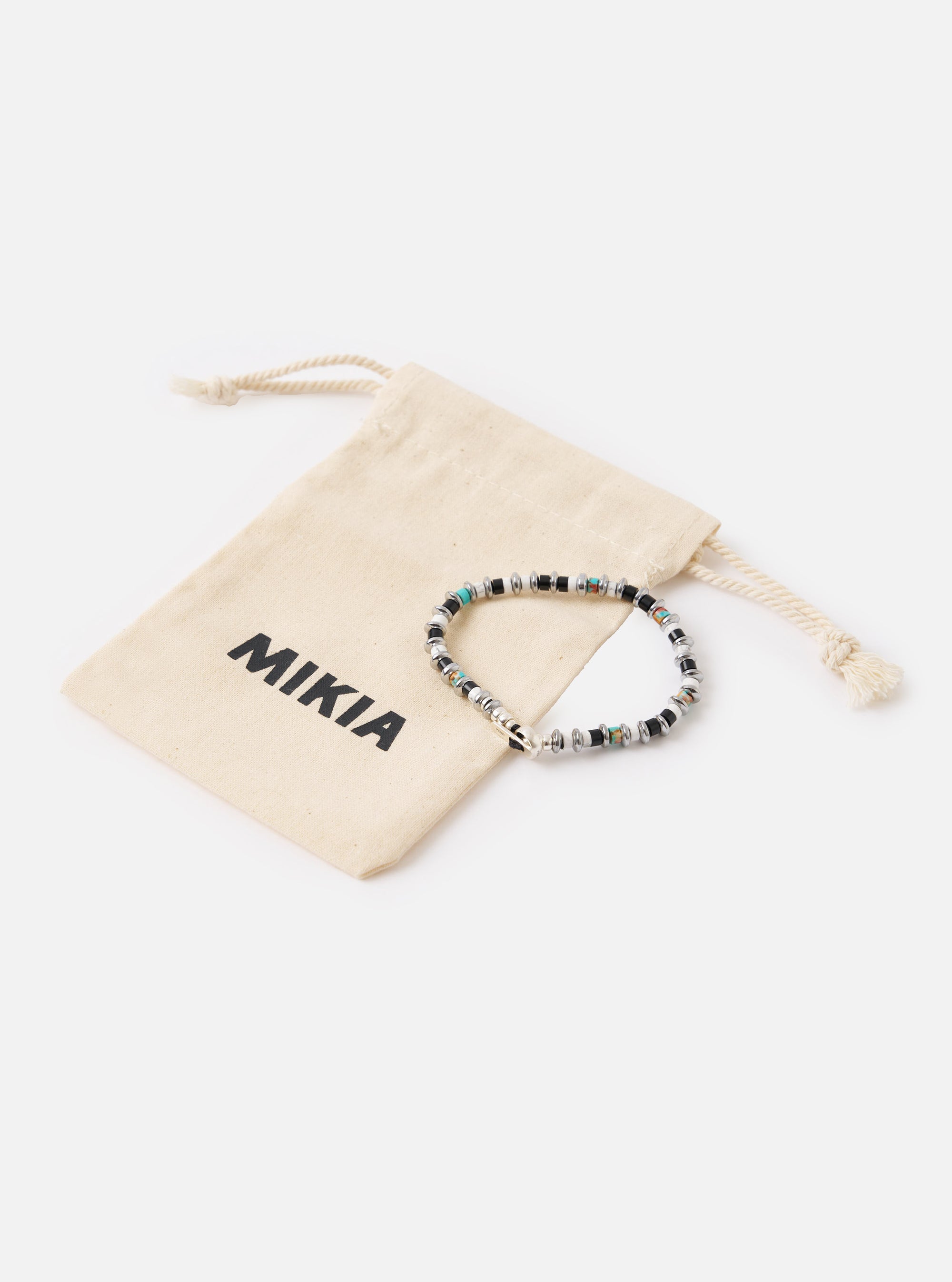 The Mikia Jet/Turquoise Hematite Roundel Bracelet on a white surface with its branded dust bag. The bracelet features jet, turquoise, and hematite beads.