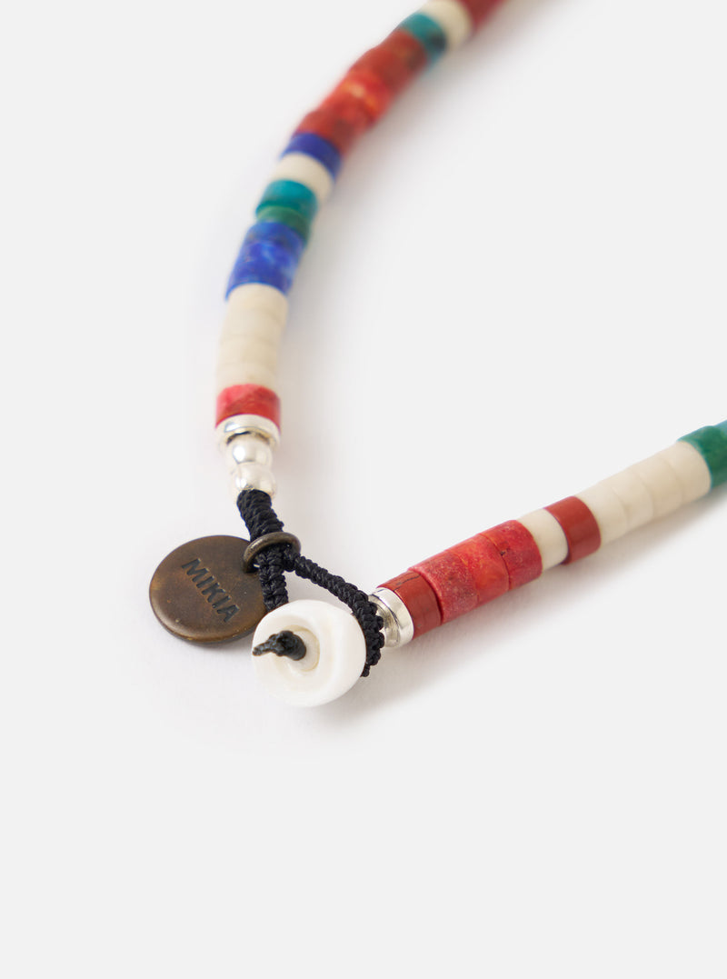 Close-up of the Mikia Safari Heishi Beads Bracelet on a white surface. Features colorful heishi beads, silver accents, and a Mikia logo charm.