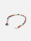 The Mikia Safari Heishi Beads Bracelet on a white surface. The bracelet features colorful heishi beads in red, blue, green, and white. It has a bronze Mikia logo charm.