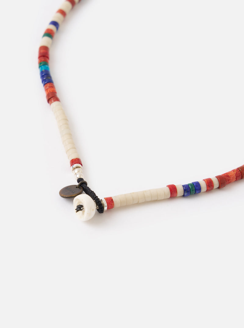 Close-up of the Mikia Safari Heishi Beads Necklace on a white surface. Features colorful beads (red, blue, green, white) and a small metal Mikia tag.