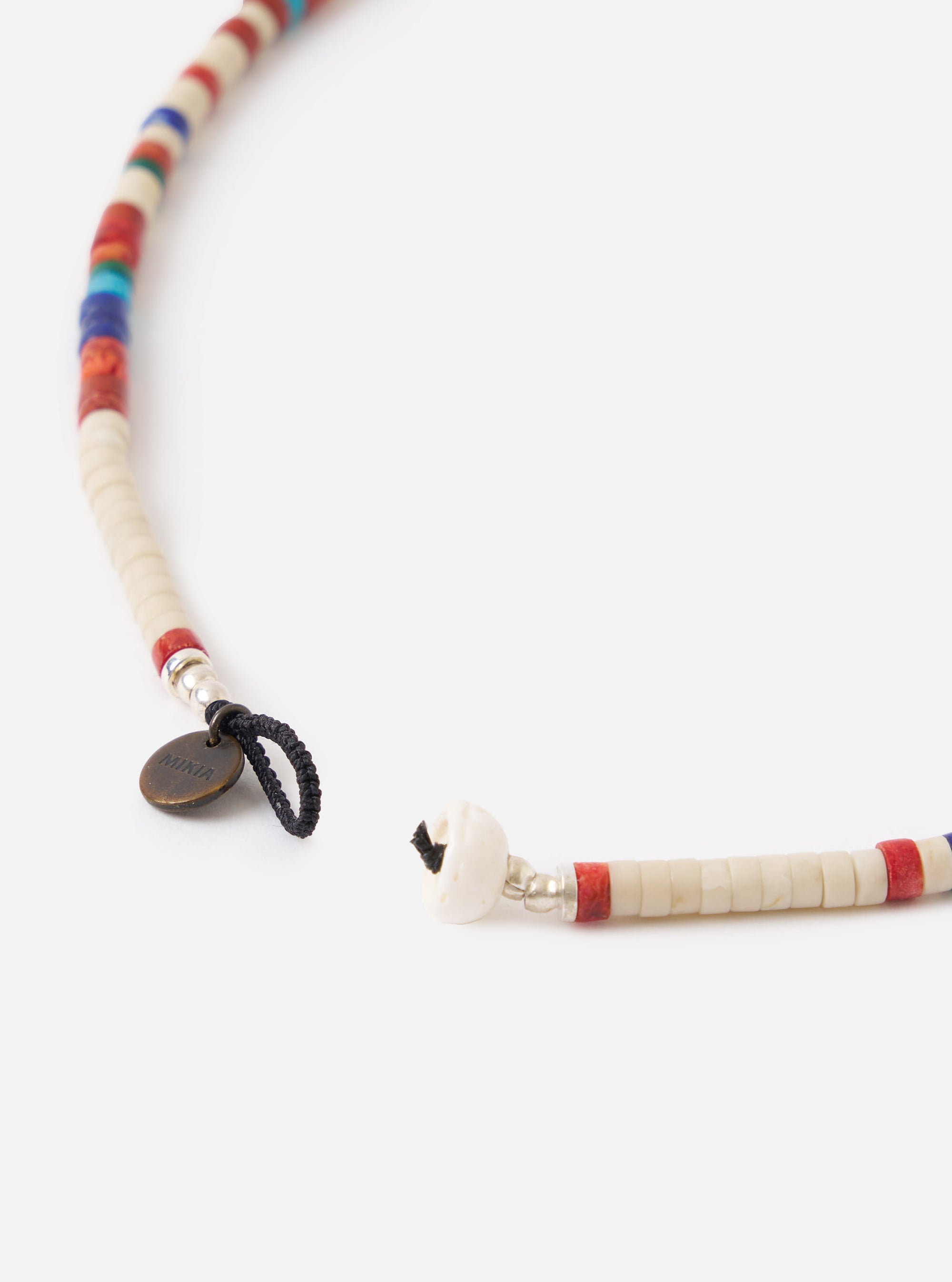 Close-up of the Mikia Safari Heishi Beads Necklace on a white background. The necklace features cream, red, and blue beads. The clasp is visible, along with the Mikia logo tag.