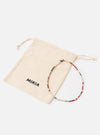 The Mikia Safari Heishi Beads Necklace with red, white and blue beads, next to its branded beige pouch on a white surface.