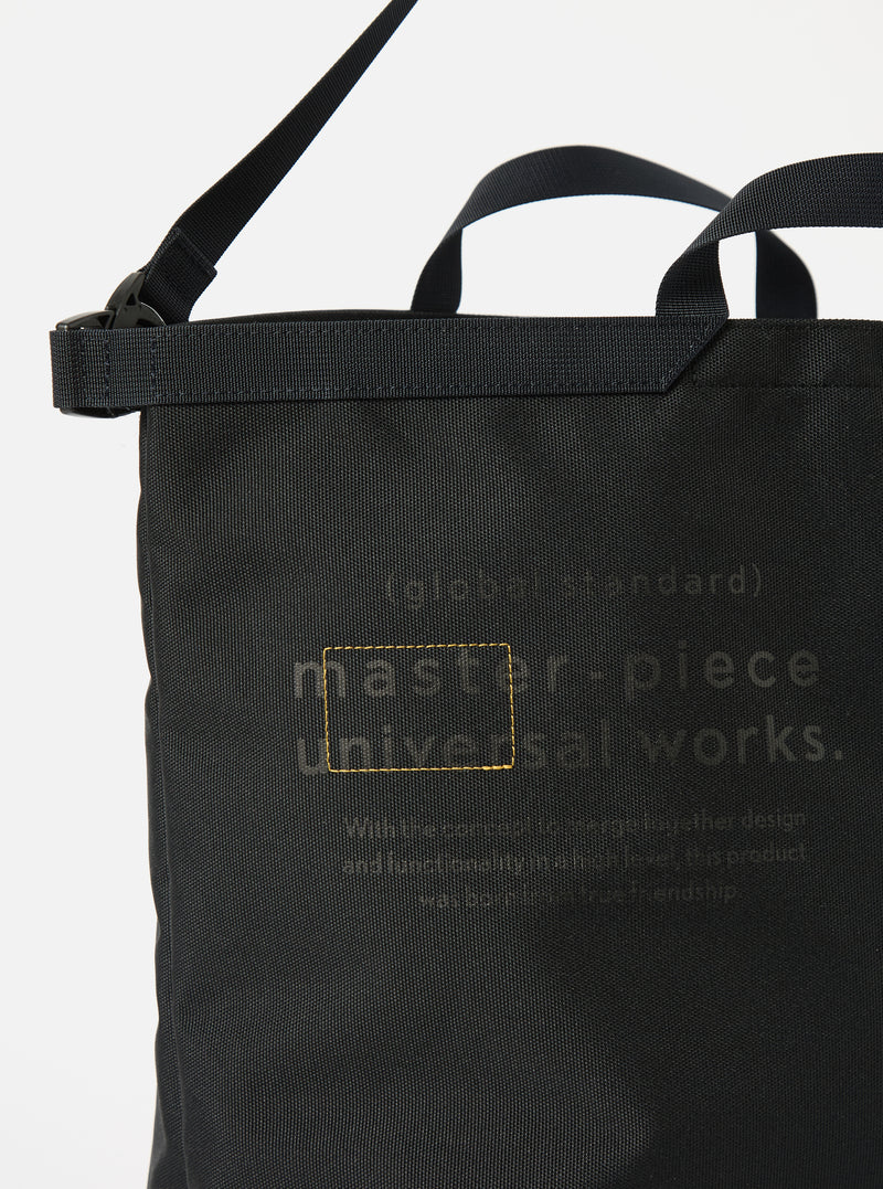 Close-up of the master-piece x Universal Works Black Recycled Tech Canvas Large Tote Bag. The black tech canvas material is visible. The bag is on a white background.