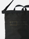 Close-up of the master-piece x Universal Works Black Recycled Tech Canvas Large Tote Bag. The black tech canvas material is visible. The bag is on a white background.