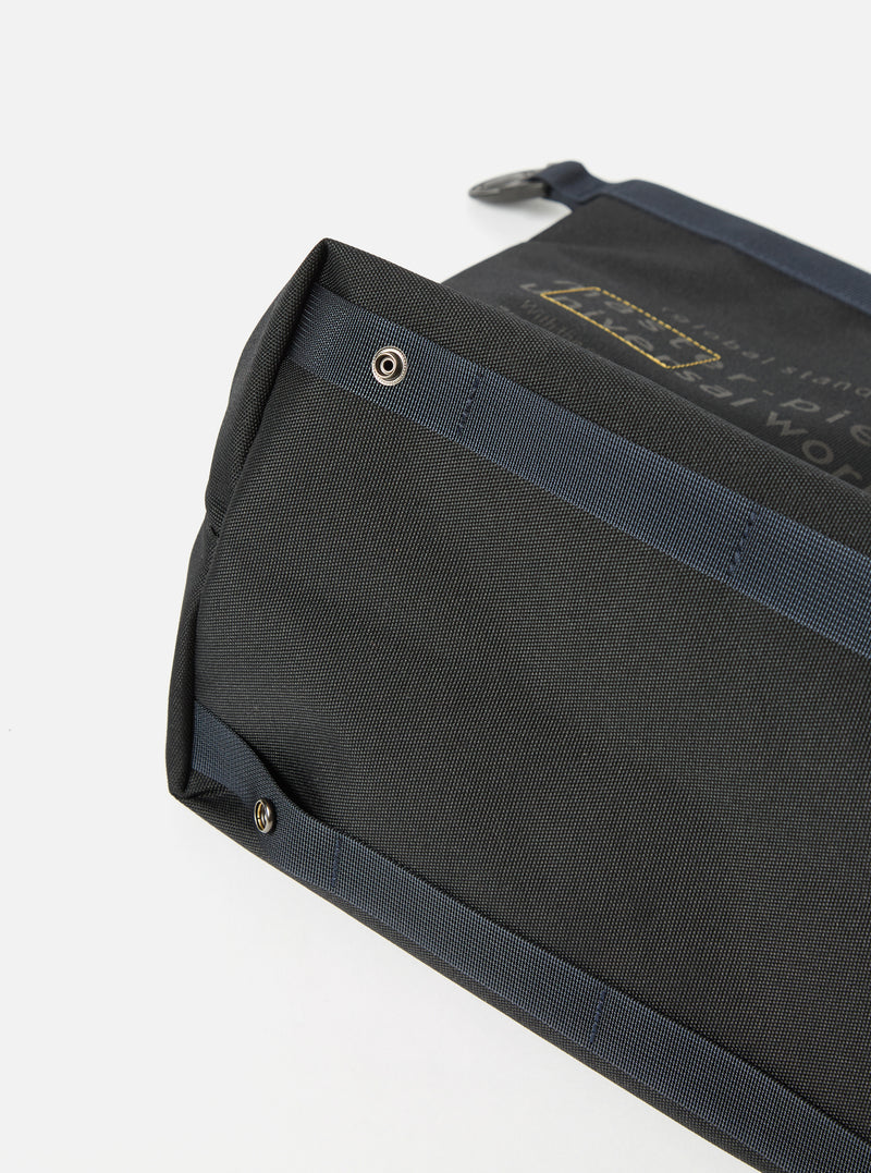 Close-up of the master-piece x Universal Works Black Recycled Tech Canvas Large Tote Bag. The black tech canvas material is visible with blue straps and silver rivets. Shot on a white background.