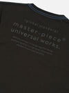 The master-piece x Universal Works Black Single Jersey Print Tee is shown from the back as a flat lay against a plain white background. The image features a large graphic print centered on the upper back, which includes the word master-piece in a stylized font above smaller text and a collaboration logo. The t-shirt is a short-sleeved crew neck made from black cotton fabric with a smooth finish.