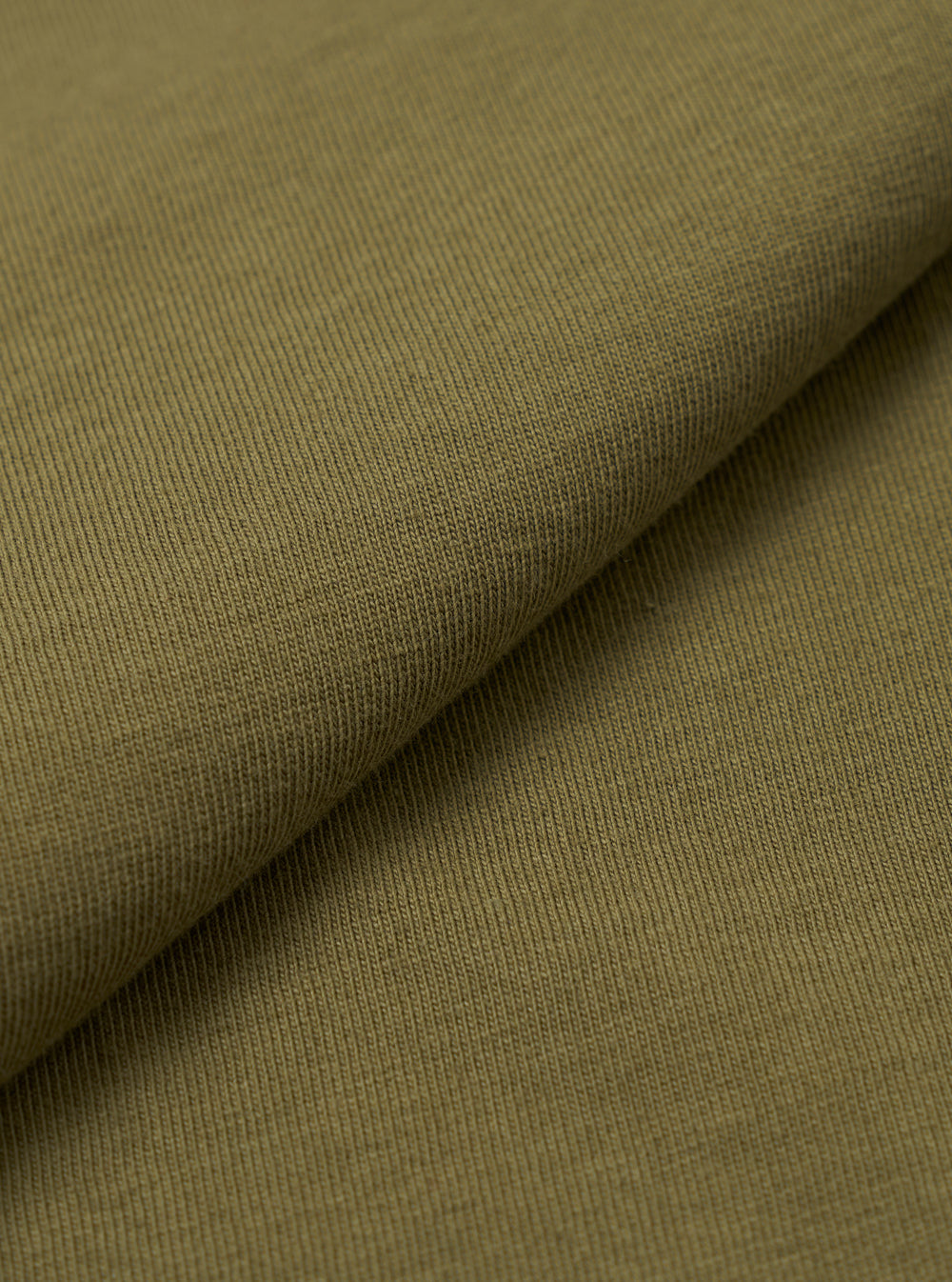 A close-up swatch image of the master-piece x Universal Works Olive Single Jersey Print Tee fabric displays a solid olive green color with a smooth, matte finish. The fine knit texture of the single jersey cotton is visible across the frame.