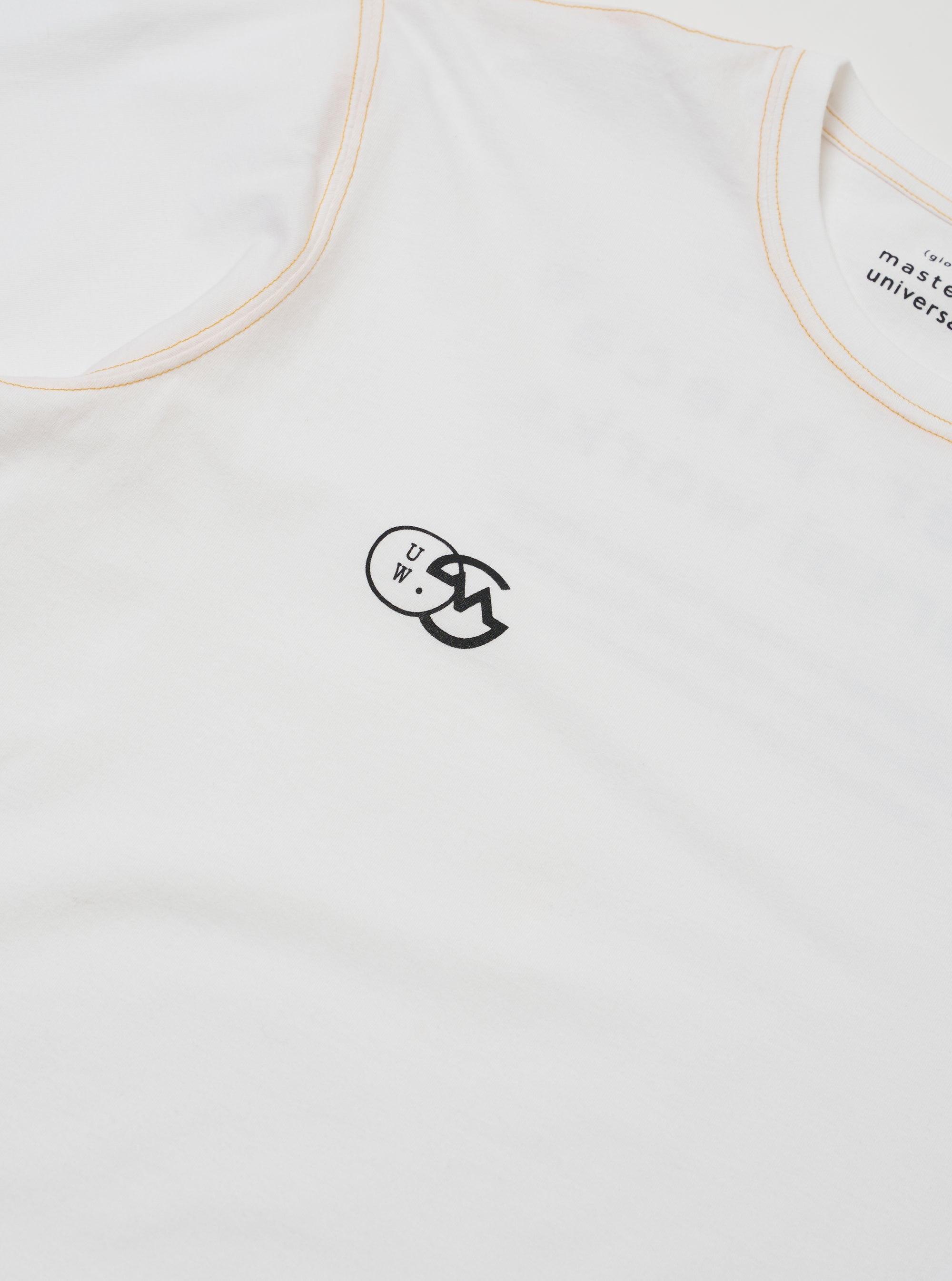The master-piece x Universal Works White Single Jersey Print Tee is shown as a flat lay against a white background. The T-shirt features a crew neckline, short sleeves, and a large graphic print on the front. The print consists of a vertical rectangular block containing various patterns, text, and illustrations in a dark ink.