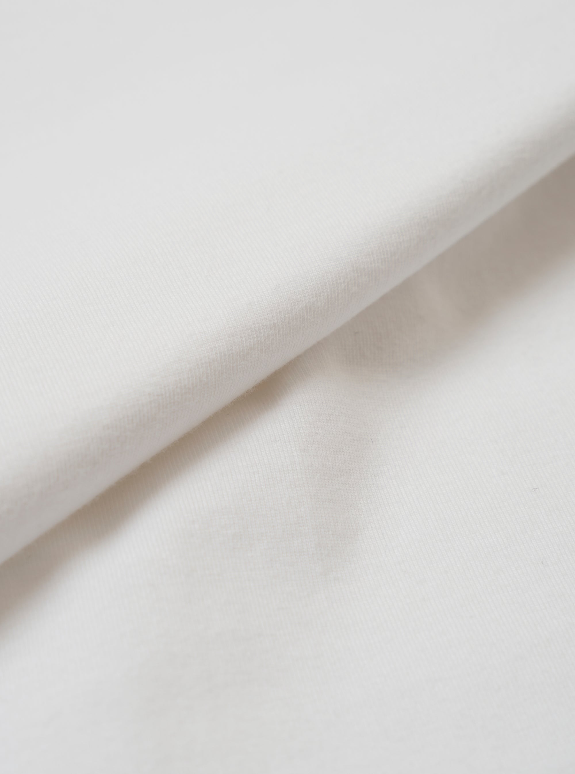 A close-up fabric swatch of the master-piece x Universal Works White Single Jersey Print Tee shows the off-white cotton material. The image focuses on the fine, smooth texture of the single jersey knit.