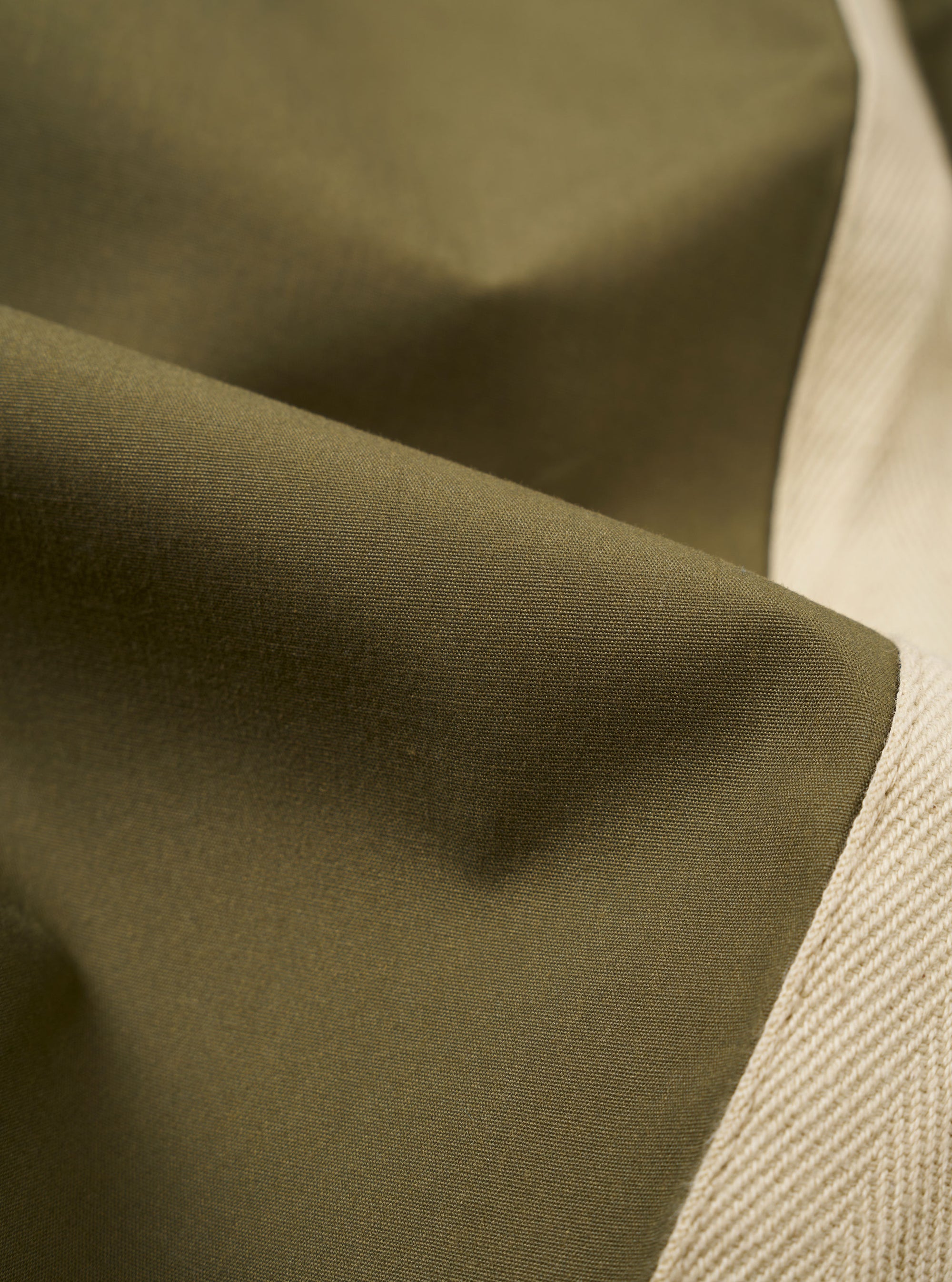The master-piece x Universal Works Olive Recycled Poly Tech Pleated Track Short is shown from a rear angle as a flat lay against a plain white background. The image highlights the two rear pockets, one of which features a button closure and a small collaborative brand tag.