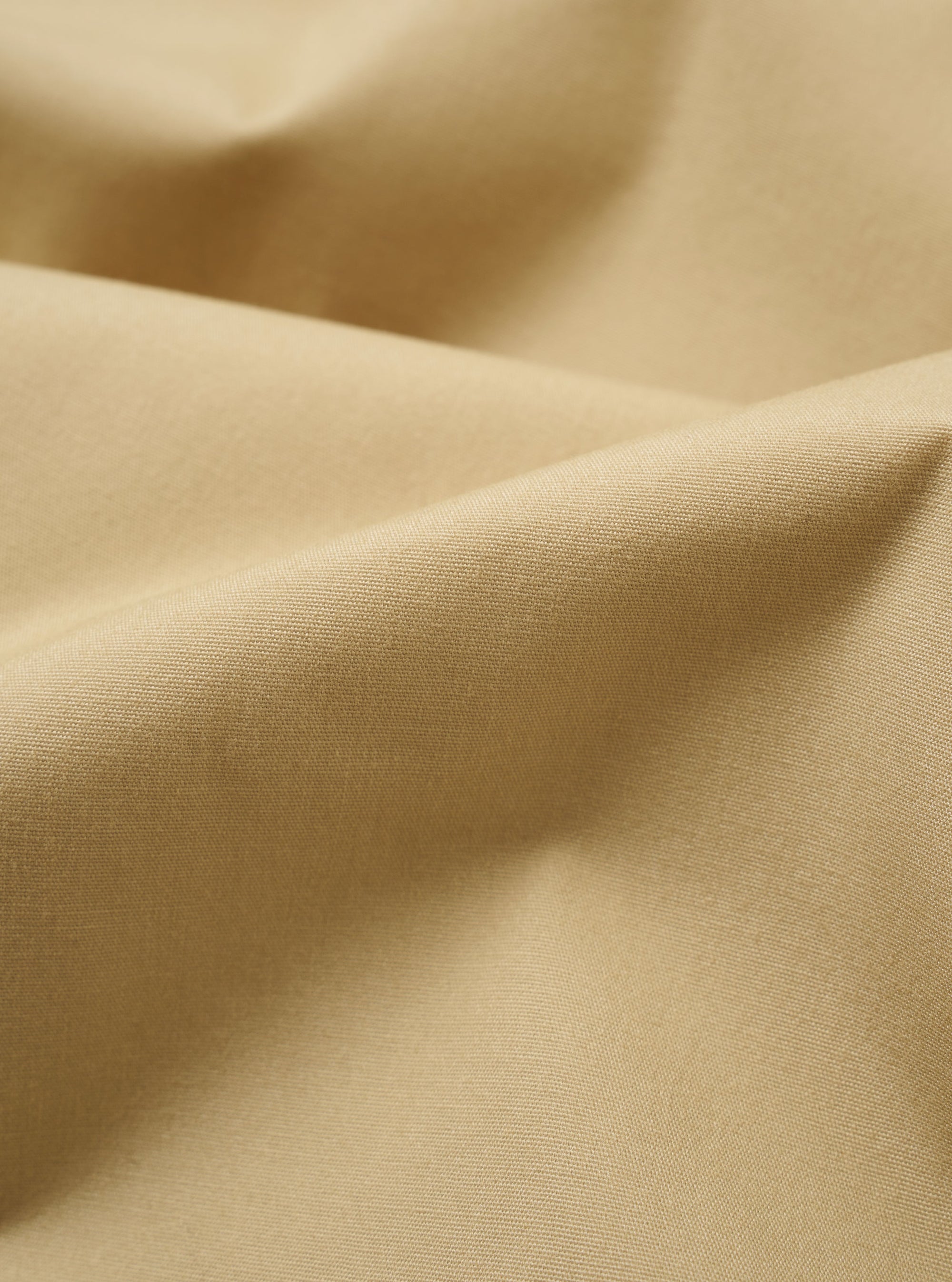 The master-piece x Universal Works Sand Recycled Poly Tech Pleated Track Short is displayed in a detail view as a flat lay against a white background. This close-up highlights the interior waistband, featuring a white collaboration label and a tan adjustable cotton drawstring. The sand-colored fabric has a clean, utilitarian appearance with visible stitching along the elasticated waist.