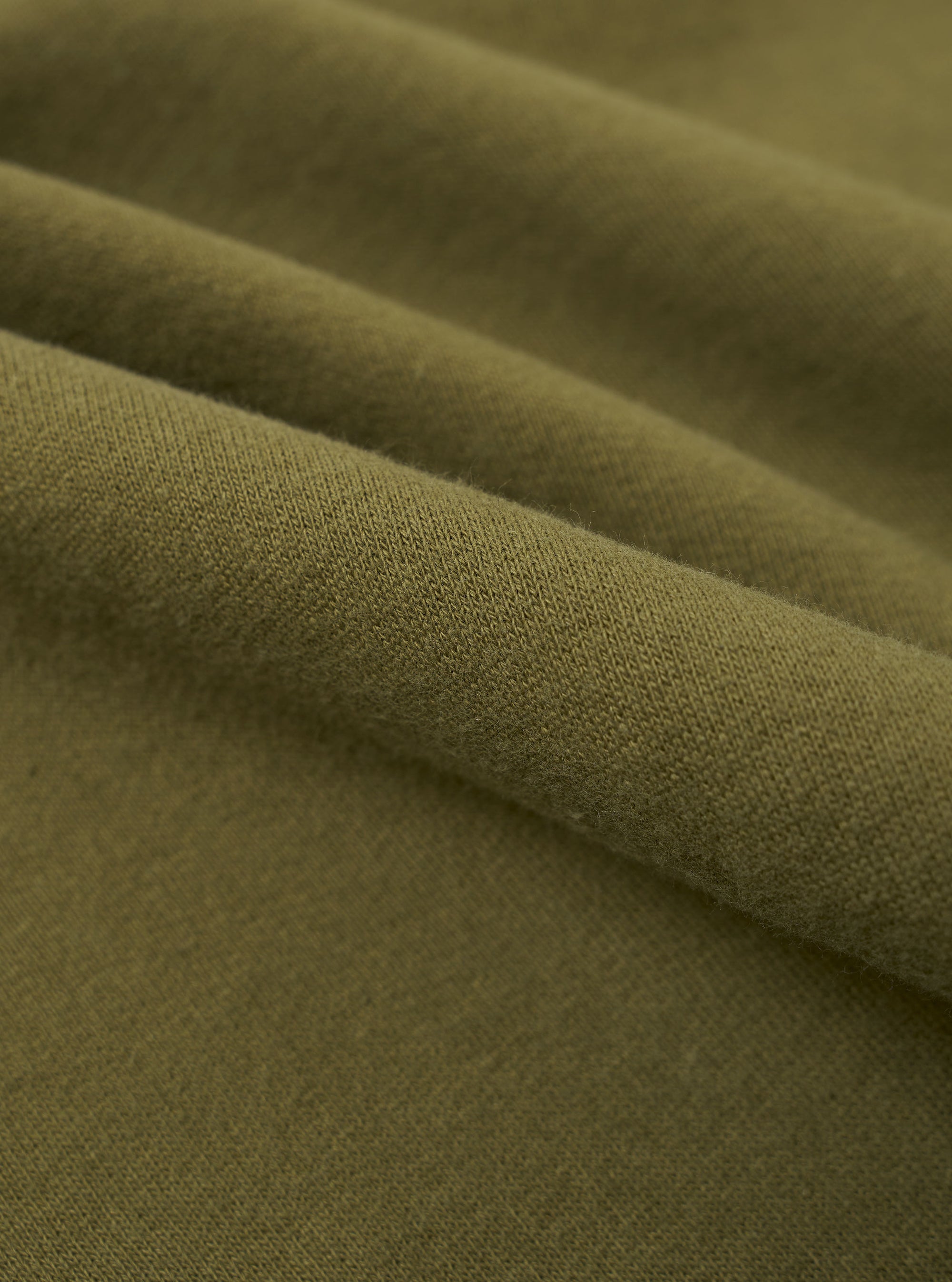 A close-up fabric swatch of the master-piece x Universal Works Olive Brush Back Sweat S/S Billy Sweat. The image displays the olive green color and the soft, textured surface of the brush back sweat fabric. No model or mannequin is present.