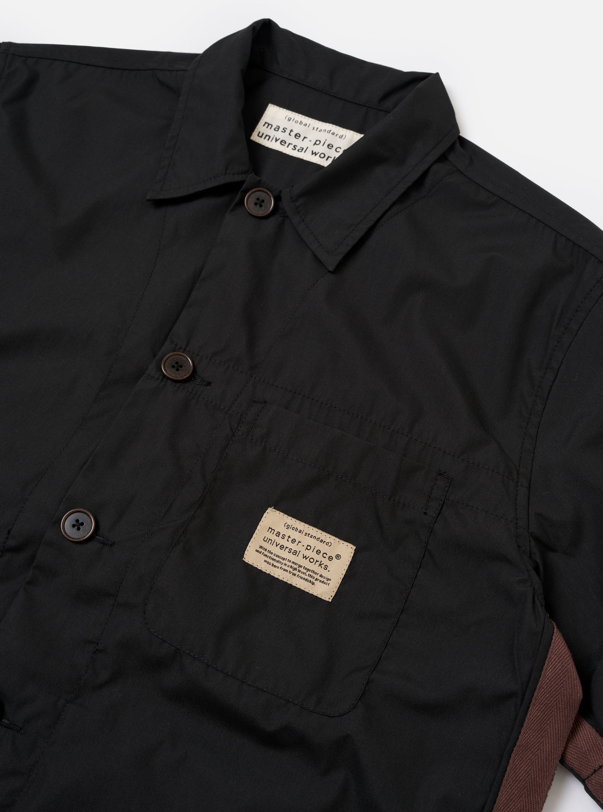 The master-piece x Universal Works Black Recycled Poly Tech Tech Overshirt is shown from the back as a flat lay against a plain white background. The image highlights the back yoke with a central box pleat and the smooth, matte finish of the black recycled polytech fabric.