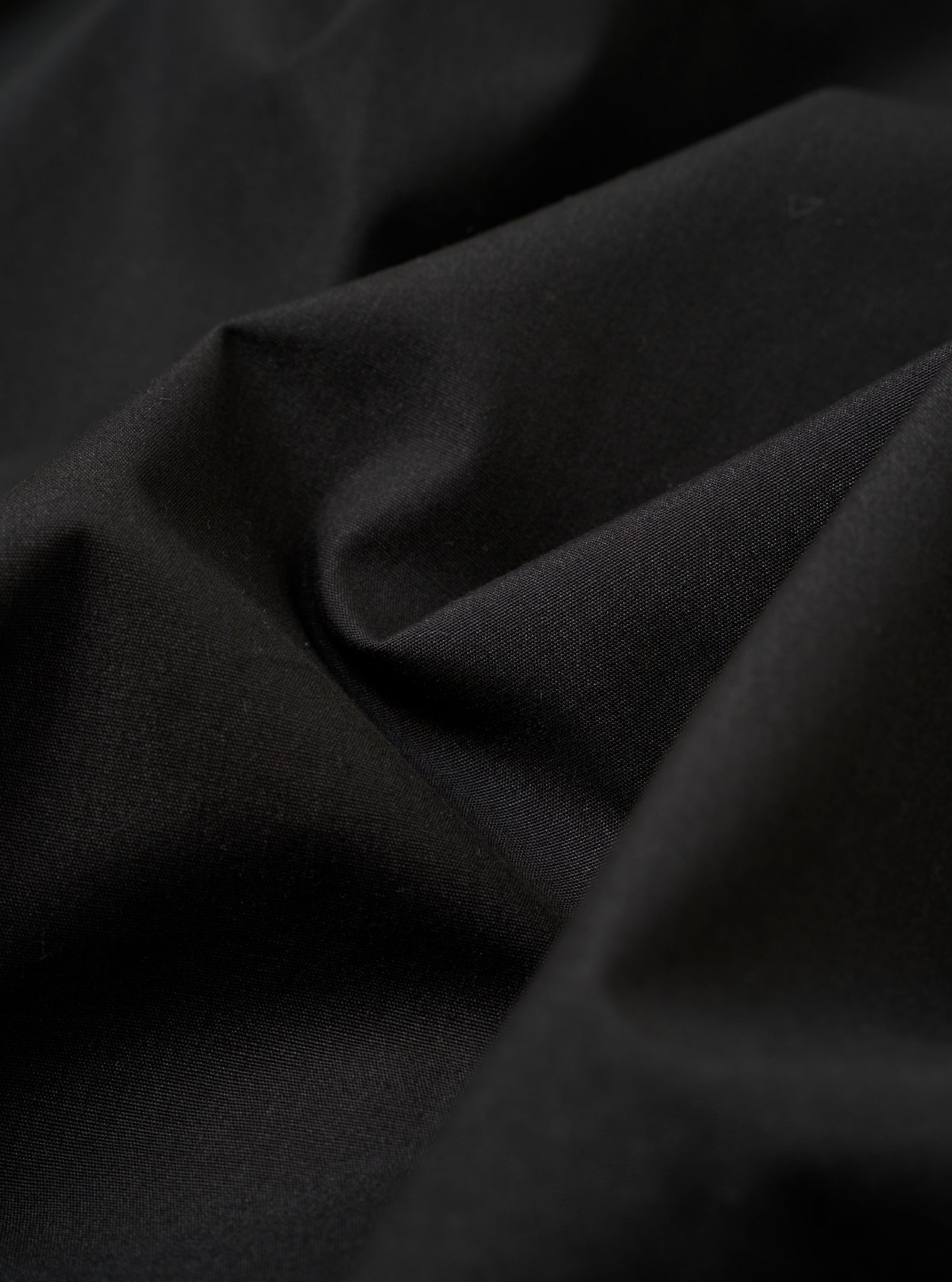 The master-piece x Universal Works Black Recycled Poly Tech Tech Overshirt is shown in a detail view as a flat lay against a plain white background. The image highlights the technical construction of the garment, specifically the reinforced chest pocket and the smooth texture of the black recycled polytech fabric.