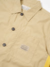 The master-piece x Universal Works Sand Recycled Poly Tech Tech Overshirt is shown from a rear three-quarter angle as a flat lay against a plain white background. The image highlights the back yoke with a box pleat, the short sleeves, and the straight hem with an adjustable elastic drawcord. The sand-colored recycled polytech fabric has a smooth, matte finish.