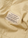 The master-piece x Universal Works Sand Recycled Poly Tech Tech Overshirt is shown in a detail view as a flat lay against a plain white background. The image focuses on the upper portion of the garment, highlighting the one-piece collar, the top buttons of the front closure, and the reinforced patch chest pocket on the left side. The sand-colored recycled polytech fabric has a smooth, matte finish.