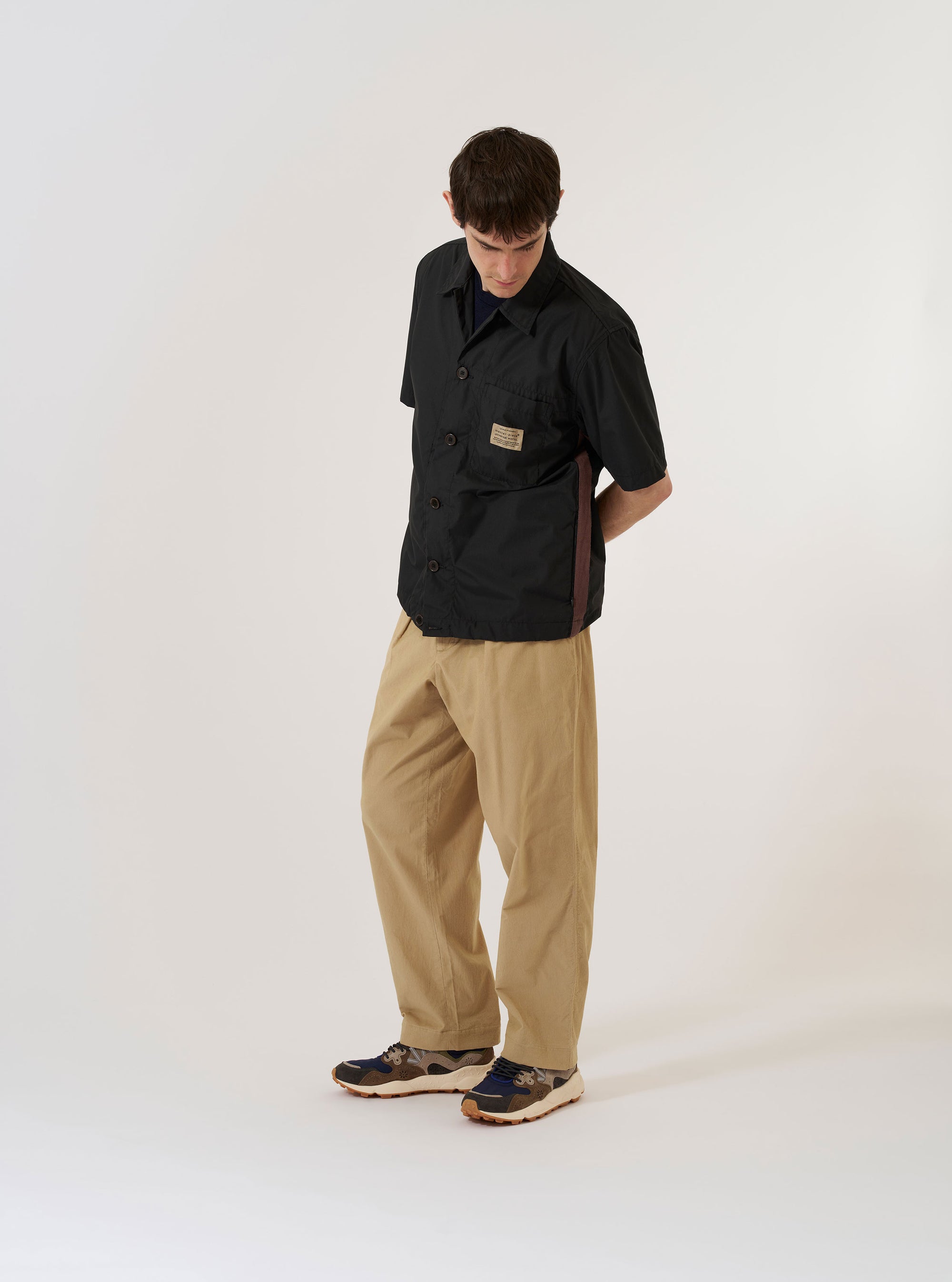 The master-piece x Universal Works Black Recycled Poly Tech Tech Overshirt is shown as a flat lay against a white background. The overshirt features a one-piece collar, a central button-down closure, and a single reinforced patch pocket on the chest. The black recycled polytech fabric has a smooth, technical finish.