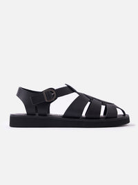 The Organic Handloom Black Leather Gurkha is shown as a flat lay against a white background. The footwear features a braided upper design with multiple black leather straps and a silver-tone buckle closure on the side. The shoe is finished with a chunky, black foam rubber outsole.