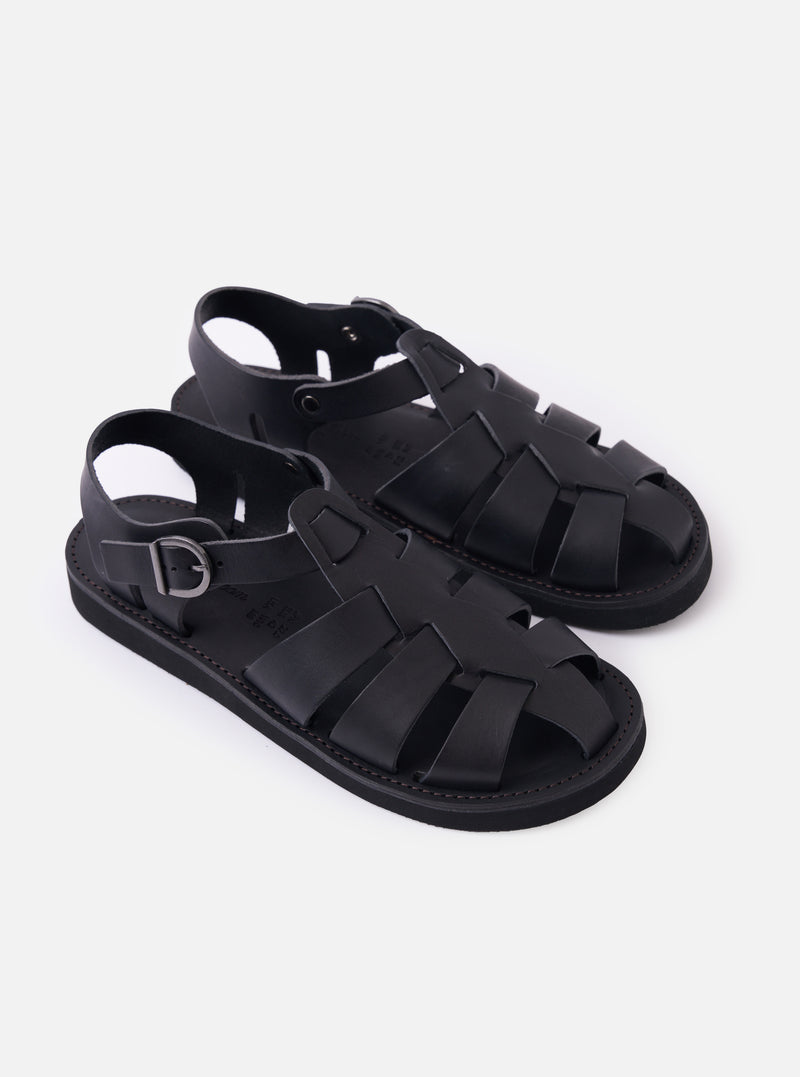The Organic Handloom Black Leather Gurkha is shown from a high-angle view as a flat lay against a plain white background. The image focuses on the top and side of the footwear, highlighting the braided black leather strap construction, the silver-tone metal buckle closure, and the thick, textured foam rubber outsole.