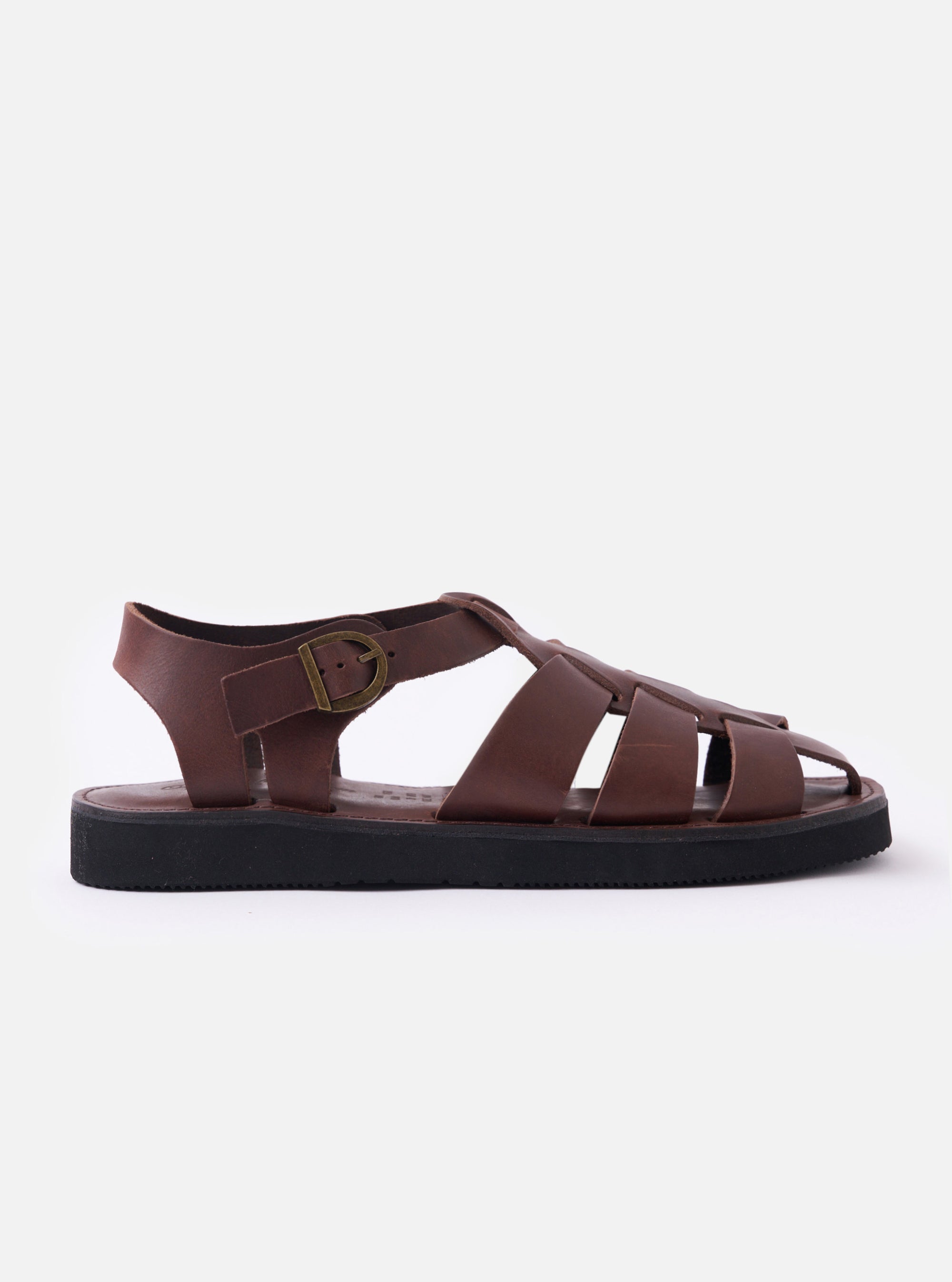 The Organic Handloom Dark Brown Leather Gurkha is shown as a flat lay against a white background. These traditional sandals feature an intricate woven leather design on the upper with a closed round toe and an adjustable side strap with a silver metal buckle. The dark brown cowhide leather has a smooth finish, and the shoe is constructed with a lightweight, black foam rubber sole.