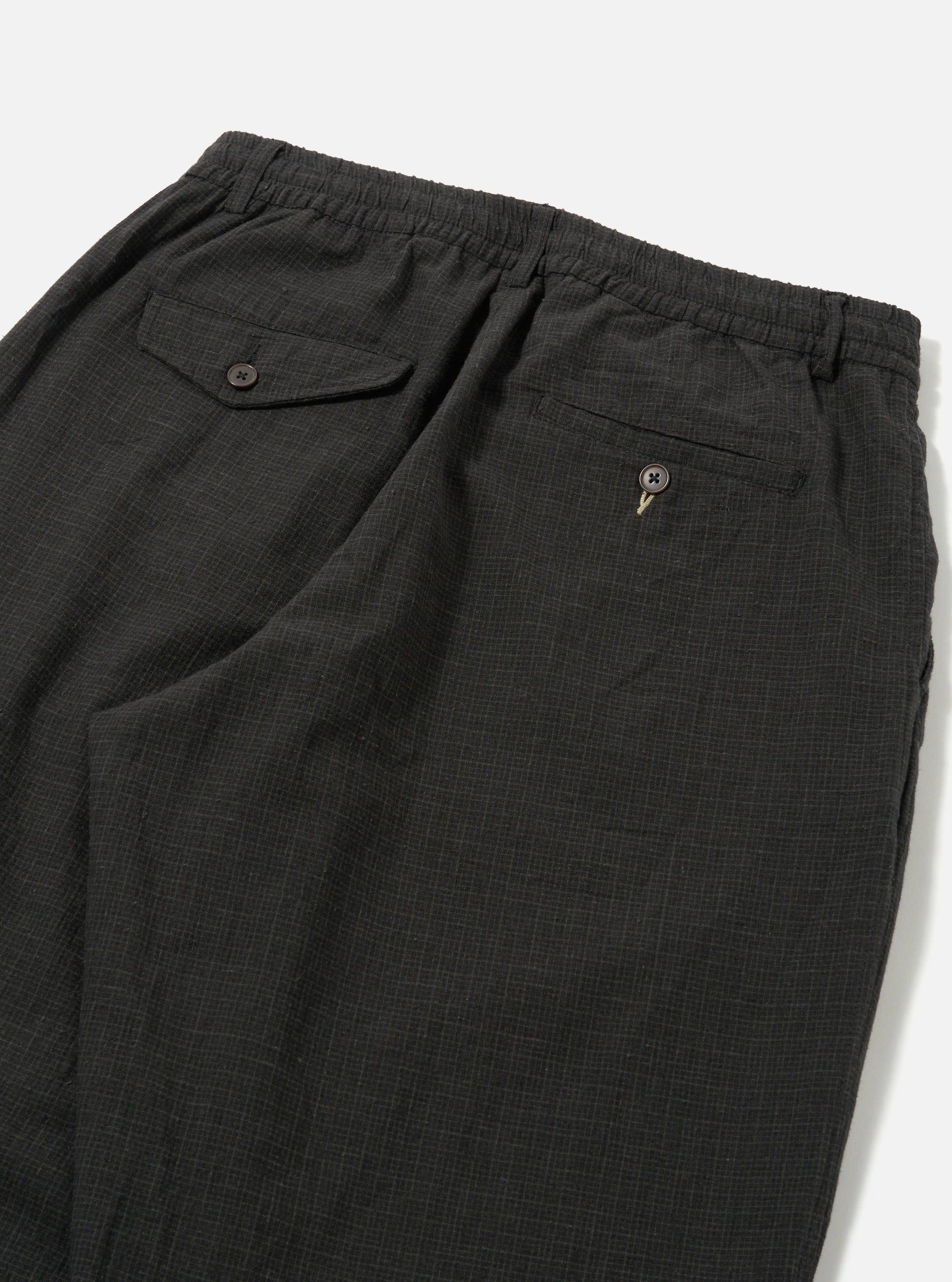 Close-up of the back of Charcoal Fine Linen Mix Pleated Track Pant on a white surface. Details include buttoned pockets and an elastic waistband.