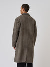 A man stands against a white backdrop, showcasing the back of a Sand Cortina Tweed Long Swing Coat. The coat features a tan and black tweed pattern.