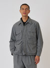 A model poses in front of a white background wearing a Charcoal Organic Chambray Parachute Field Jacket. The jacket is a light gray color and has four front pockets.