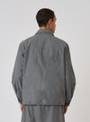 Back view of a model wearing the Charcoal Organic Chambray Parachute Field Jacket. The jacket is a relaxed fit and made of a textured charcoal fabric. The background is a plain white studio backdrop.